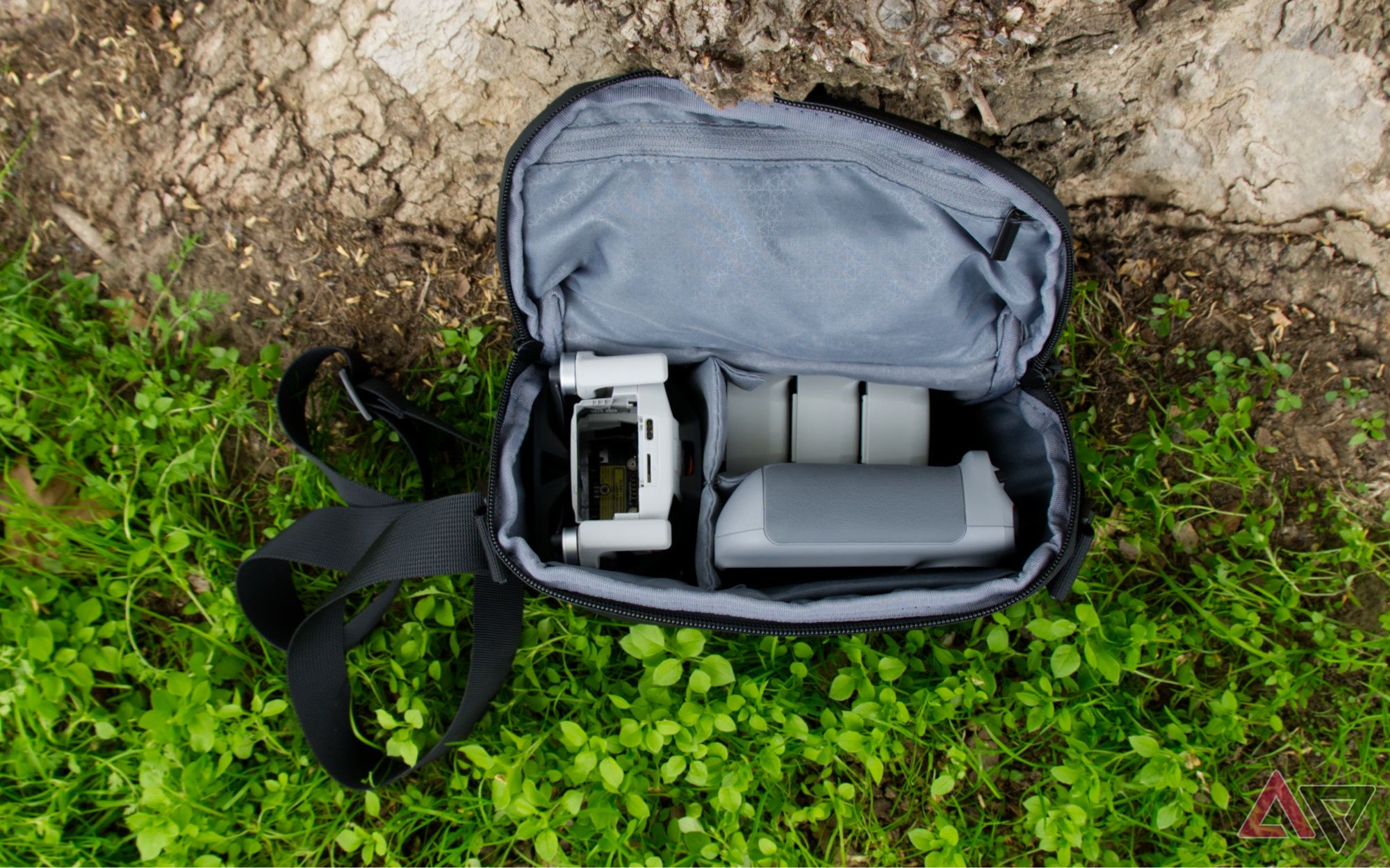 DJI Mini 4 Pro, controller, and batteries inside of the bag from the fly more kit, sitting against a tree and on the grass