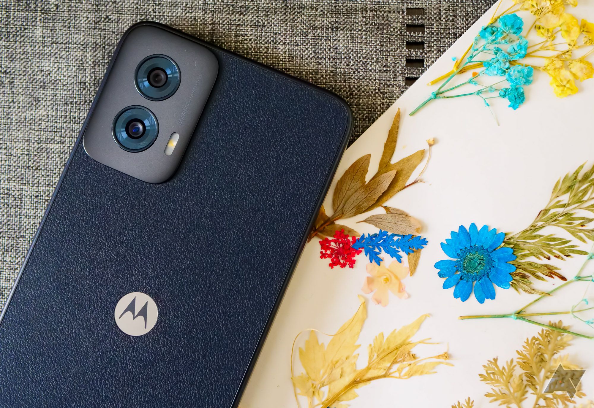 The Moto G Power (2024) lying on gray fabric and next to a flower print