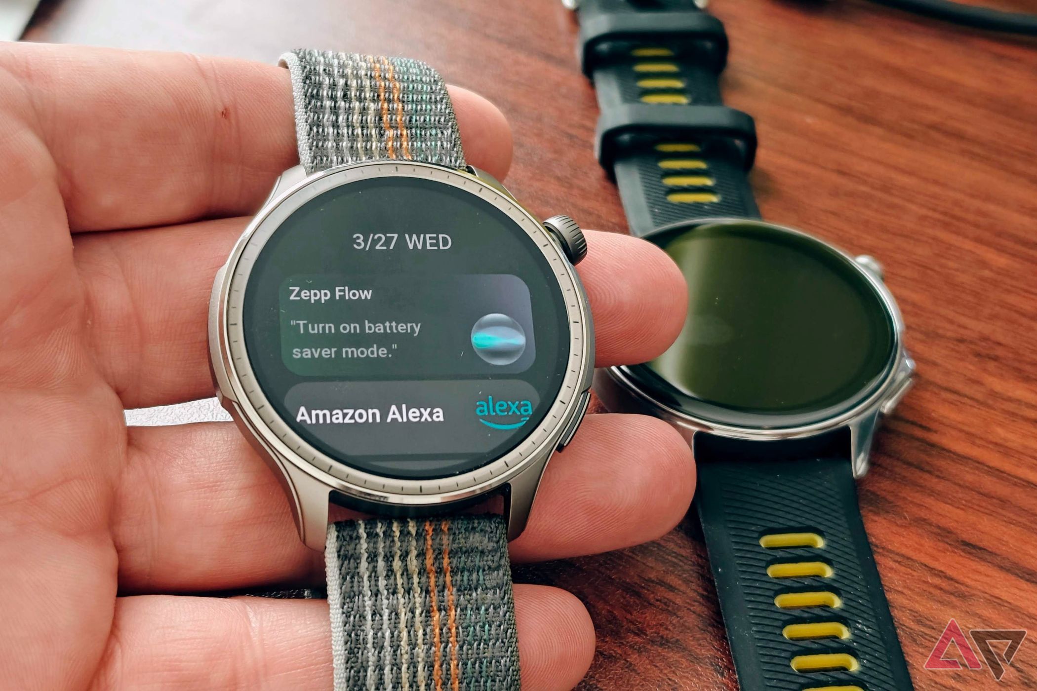 Amazfit Balance in hand showing voice assistants with OnePlus Watch 2 on a table
