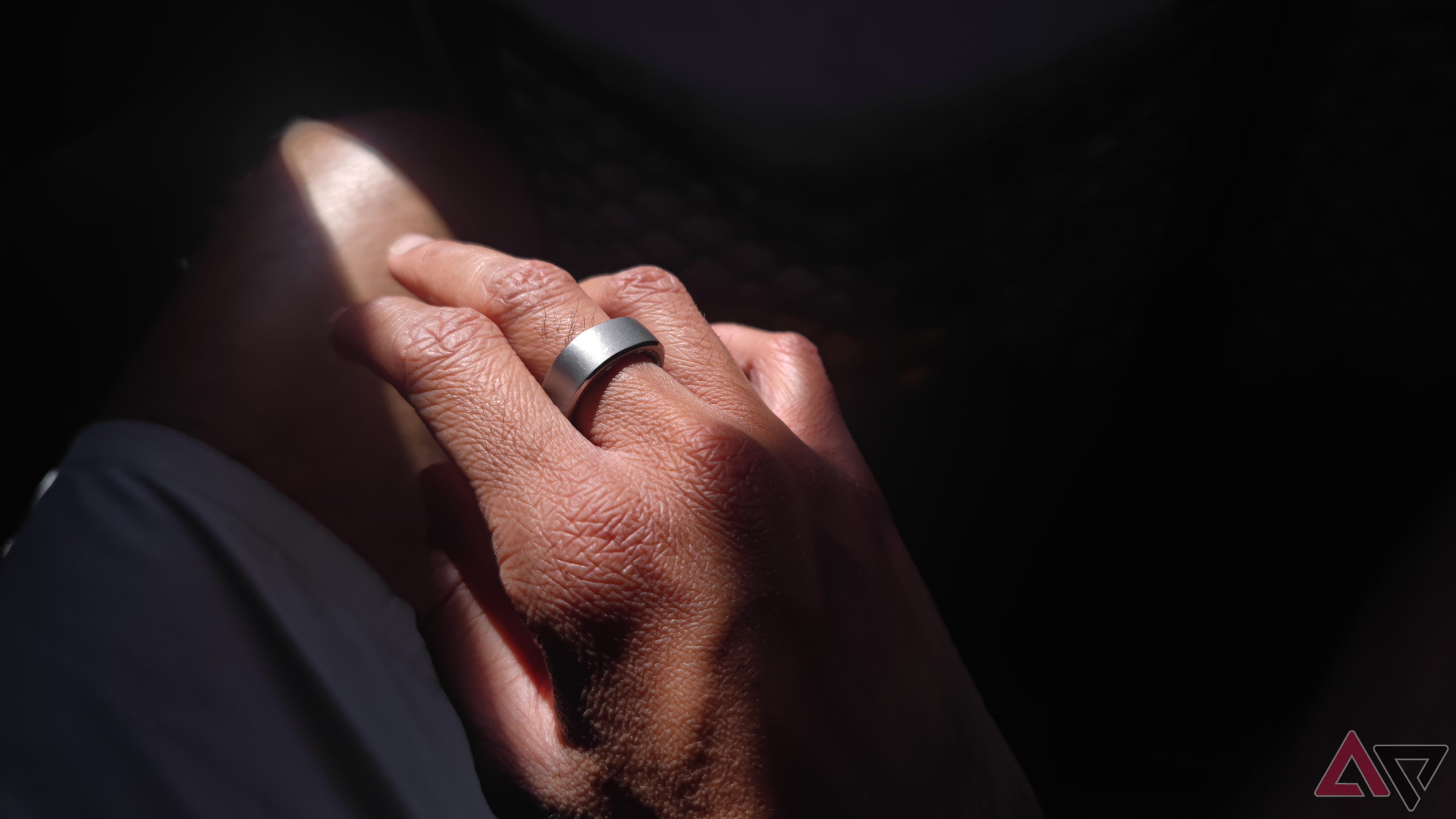 A hand wearing a silver ring in dramatic lighting