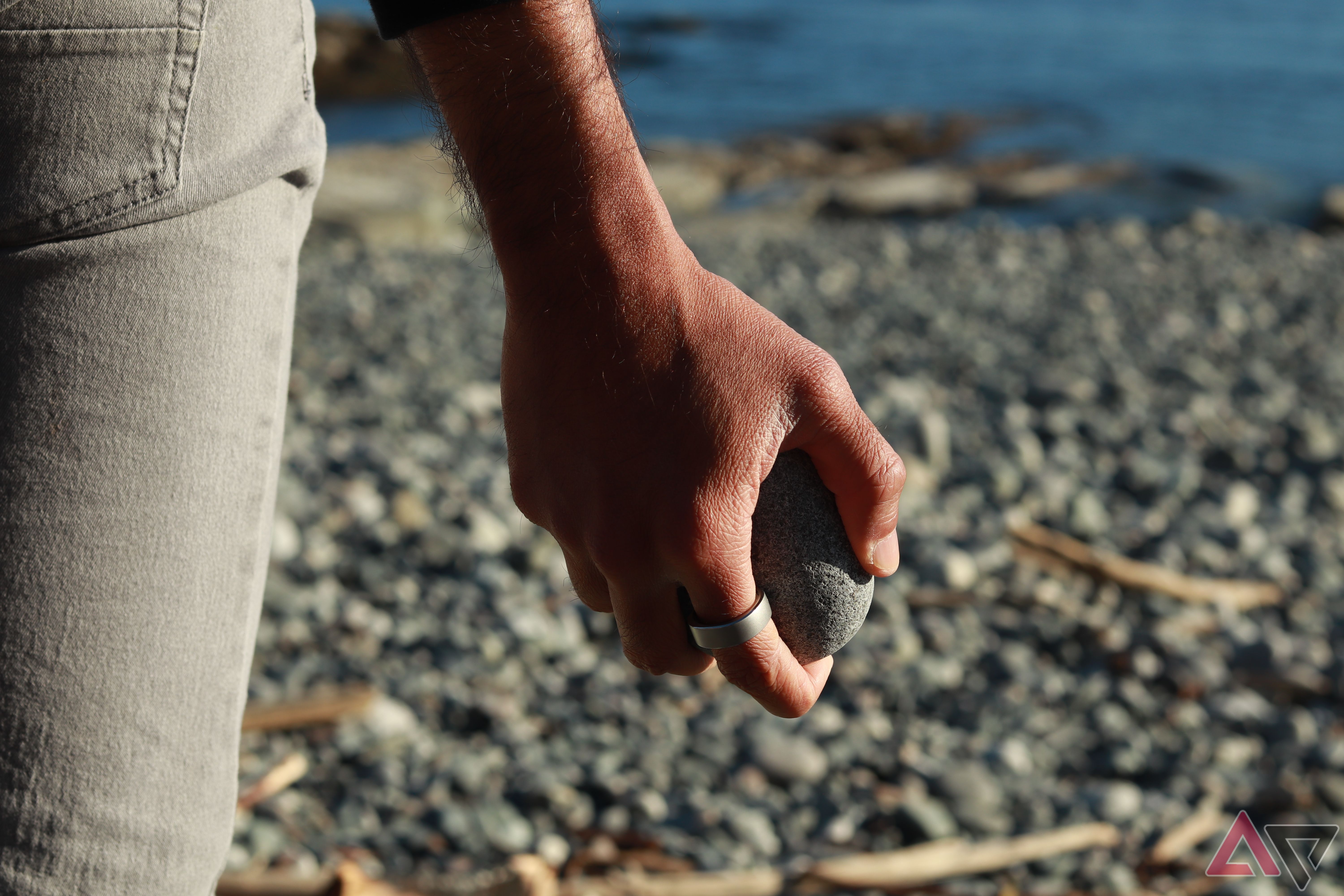 Holding a pebble at the beach with a smart ring on the finger