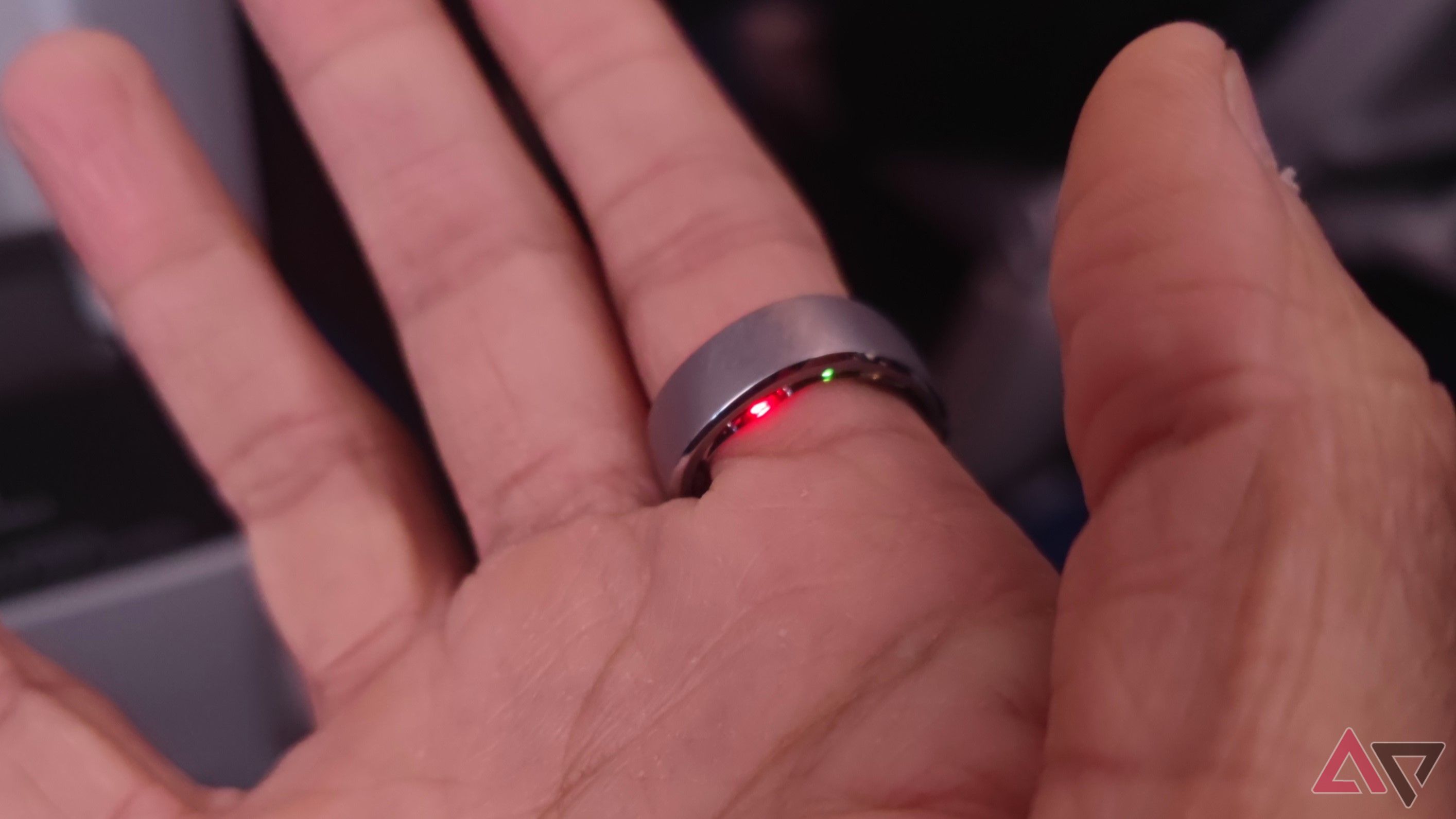 A hand wearing a smart ring with sensors illuminated