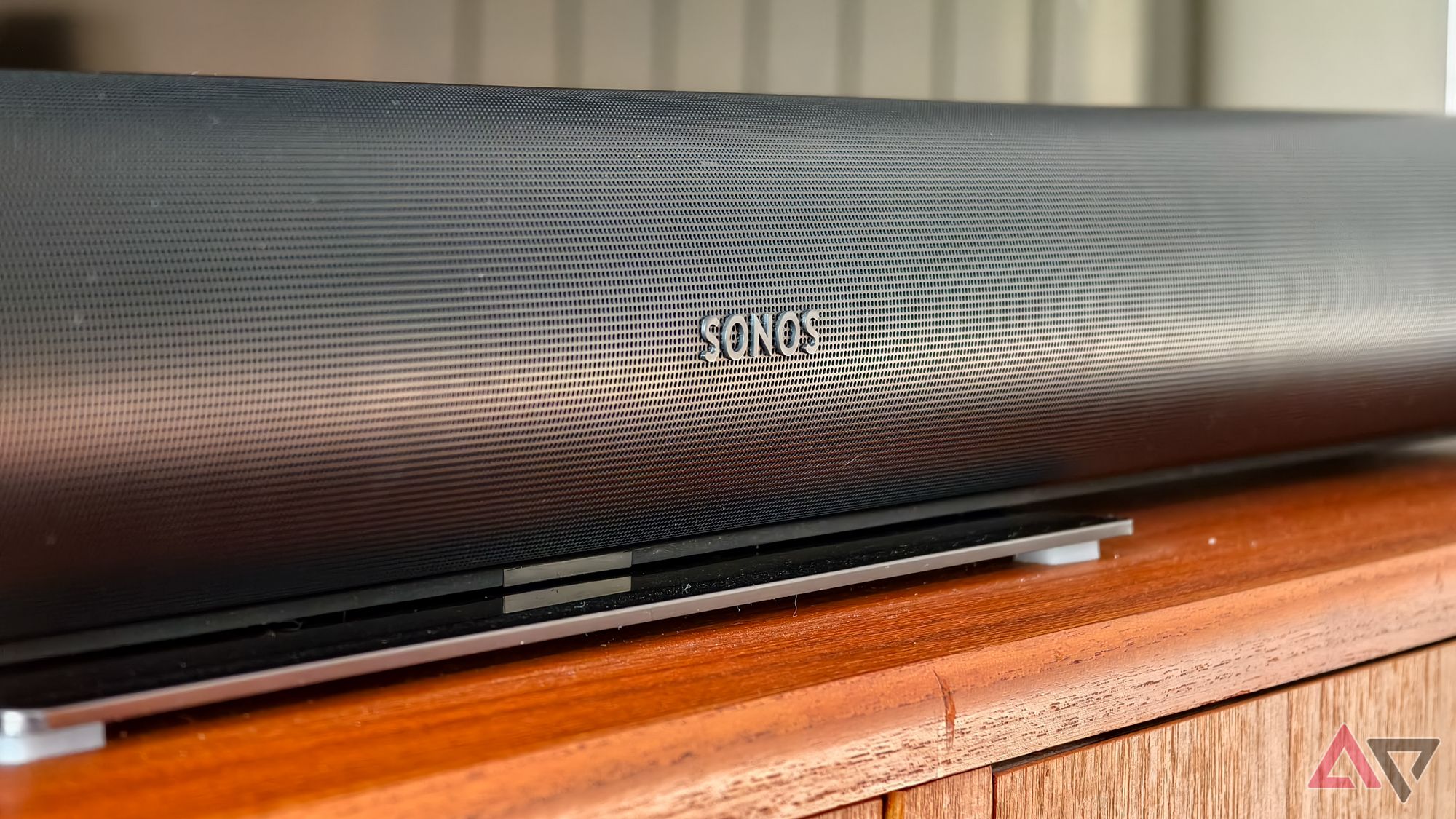 The Sonos logo visible on a black Sonos Arc soundbar on a teak TV stand