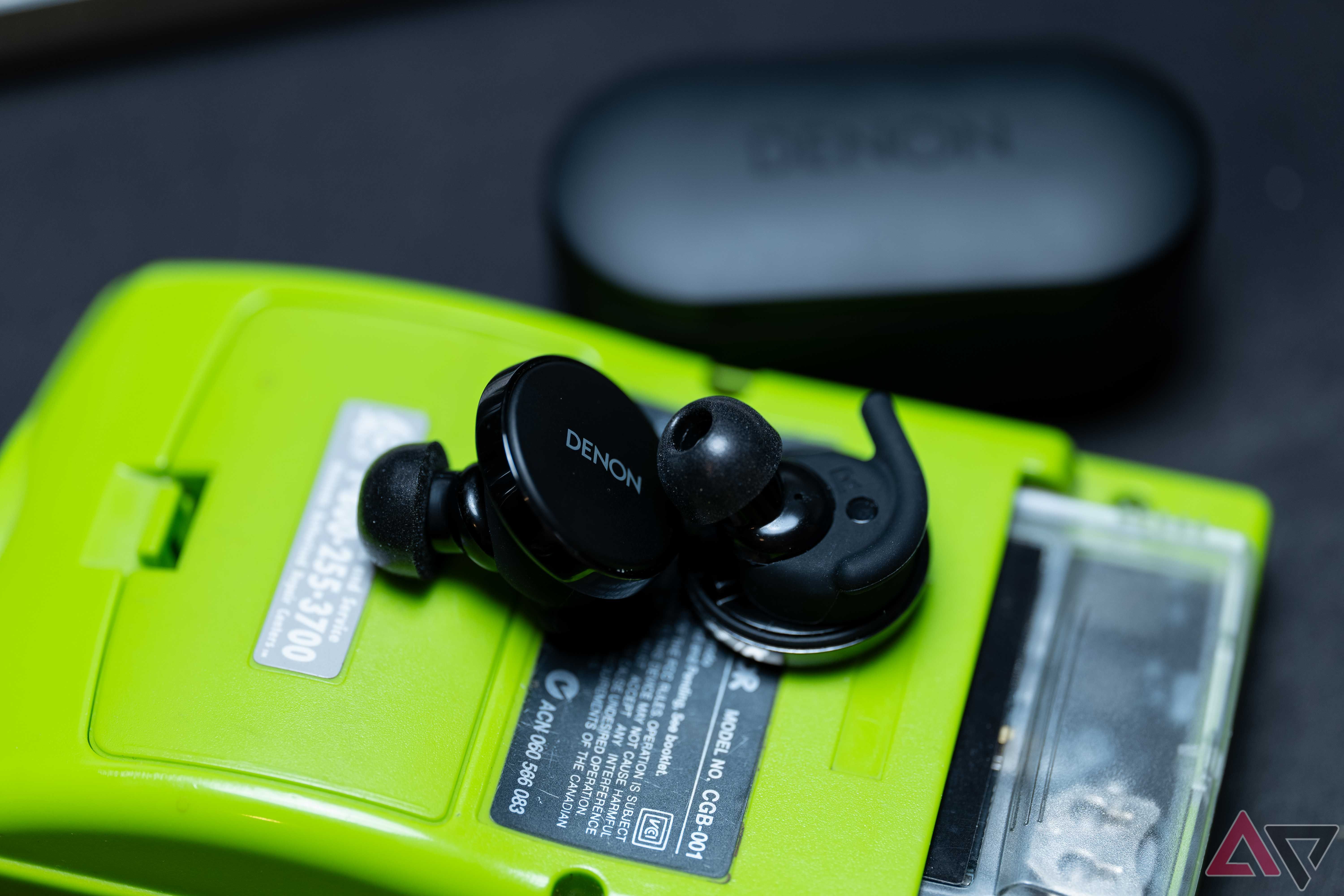 The Denon PerL Pro earbuds laid on the back of a lime green Gameboy Color, with the large wings and foam tips on the earbuds