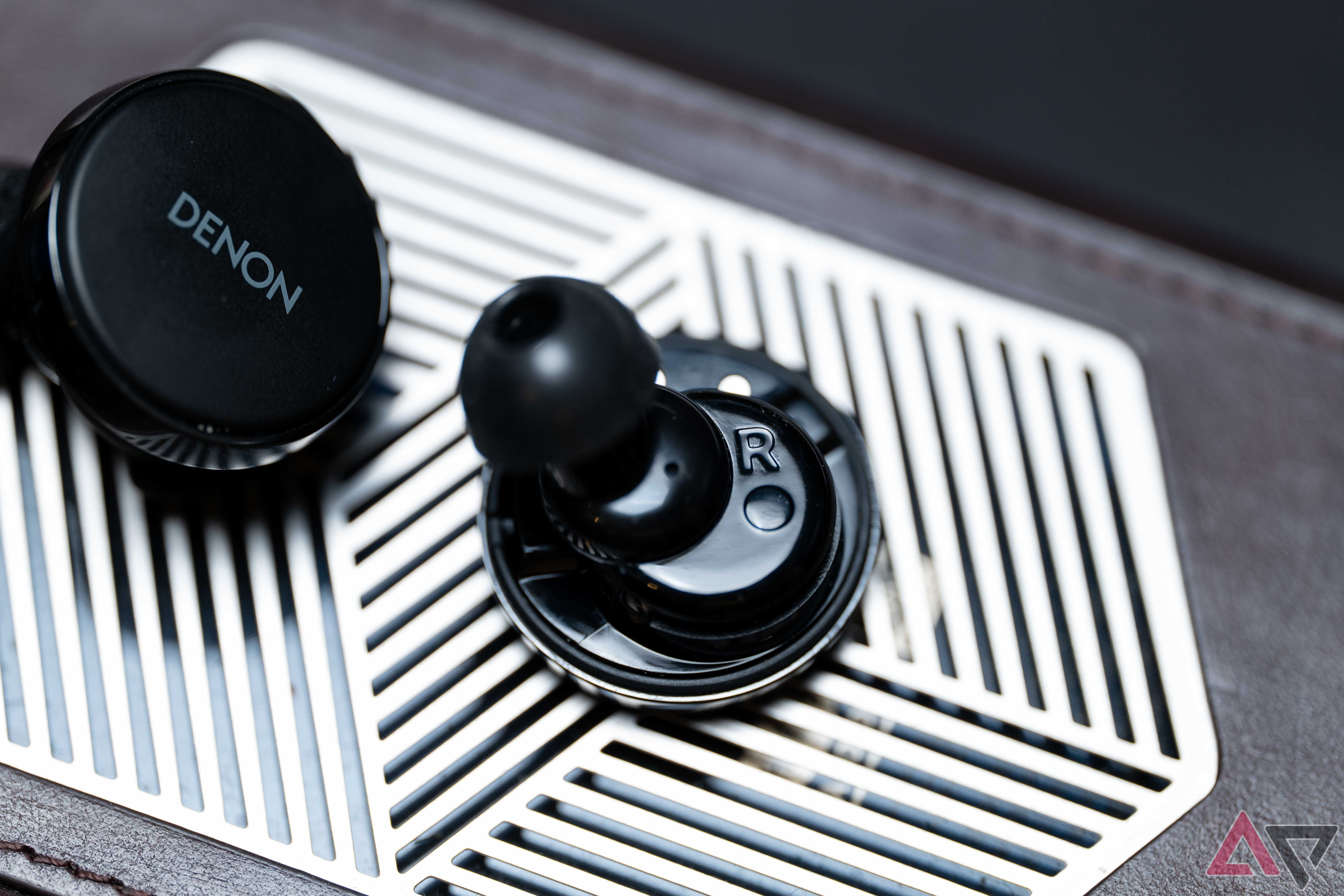 The Denon PerL Pro earbuds with no wingtips, on top of a metal plate with stylized geometric patterns of a three dimensional object