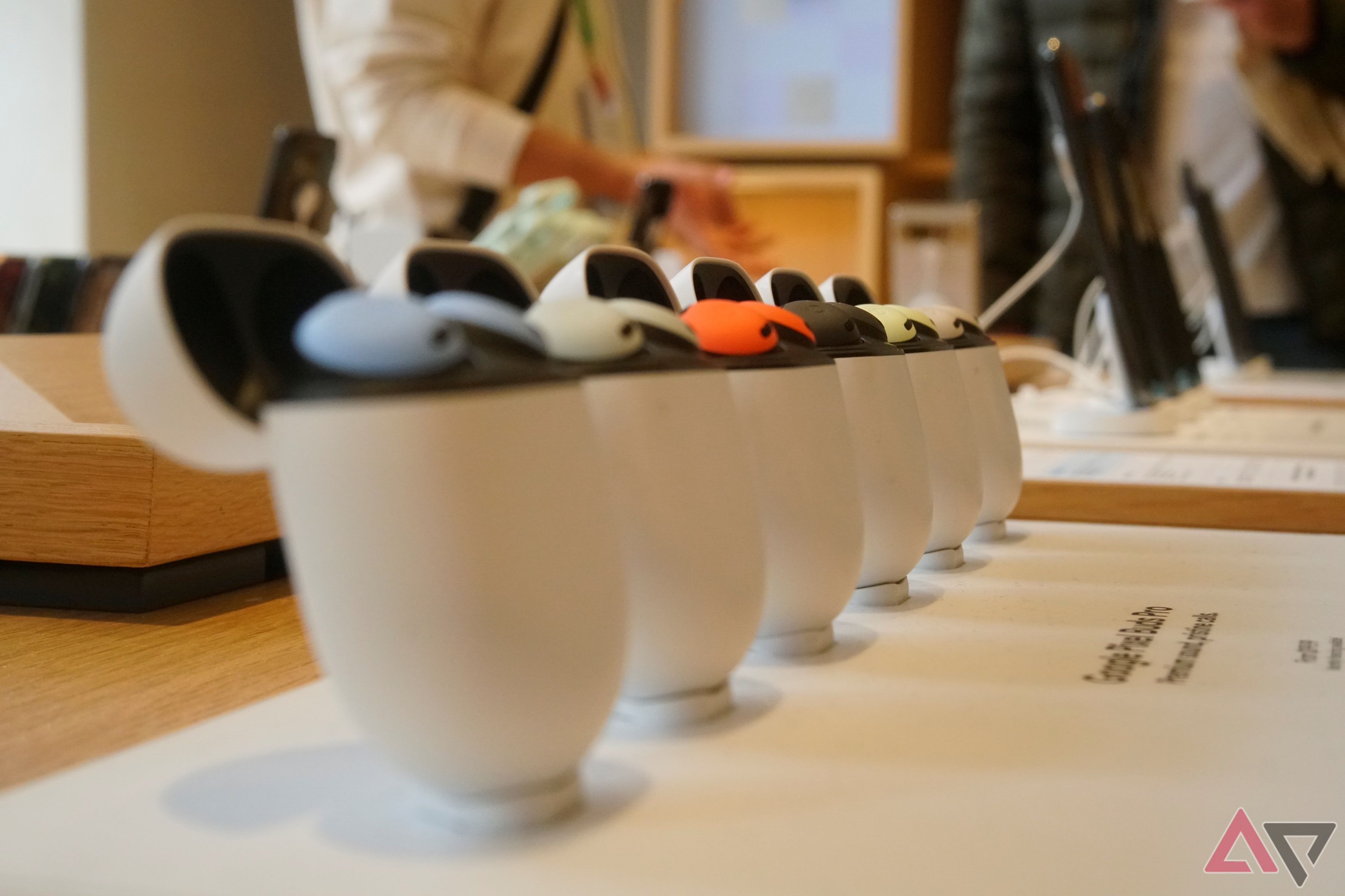 Six pairs of Google Pixel Buds Pro sat in their charging cases on a retail table.