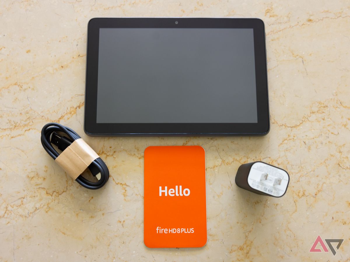 A Kindle Fire HD 8 Plus, charging cable, plug, and welcome booklet lying on a table