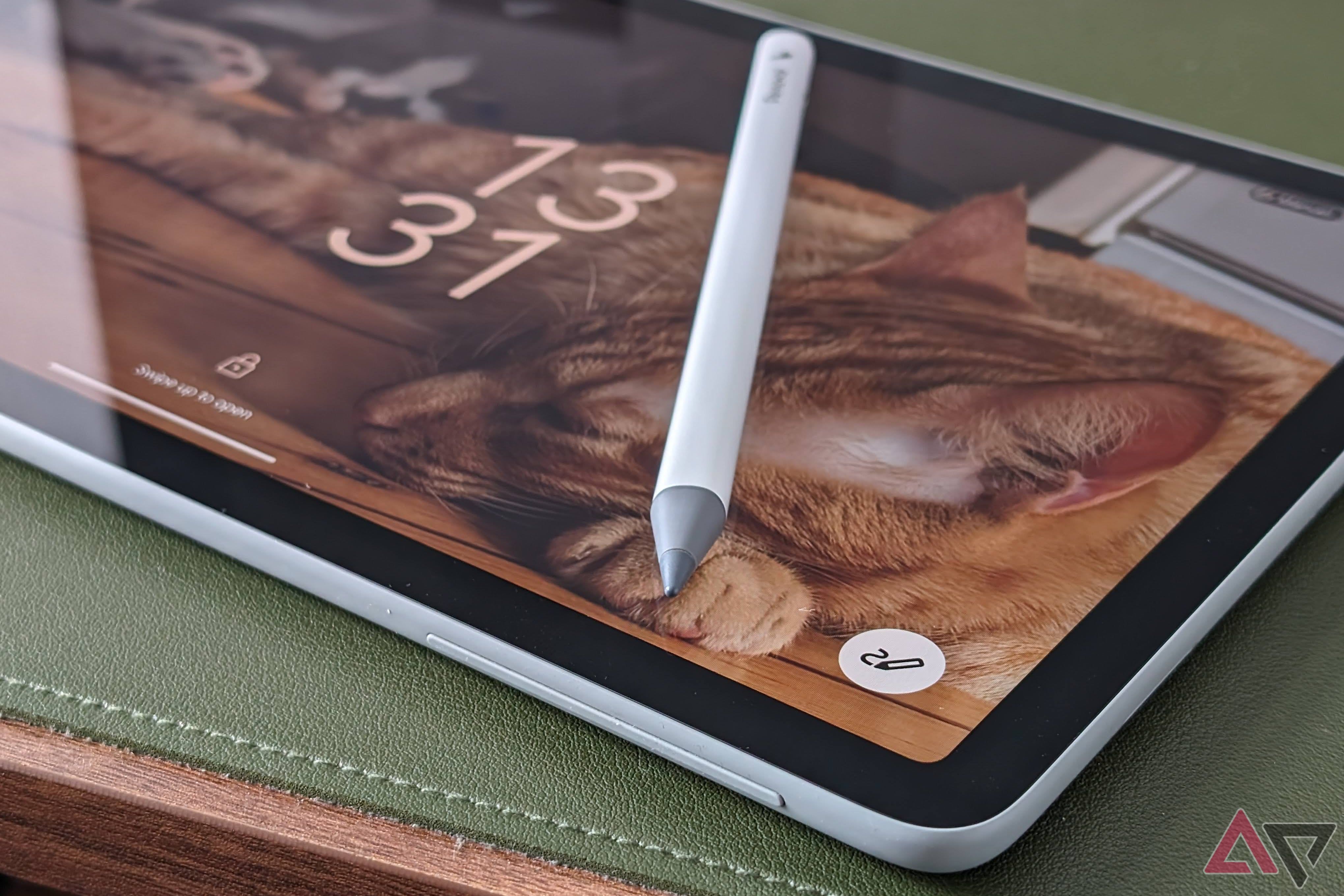 A partial look at the Google Pixel Tablet with the note button on its home screen highlighted and a third-party stylus laying on top of it