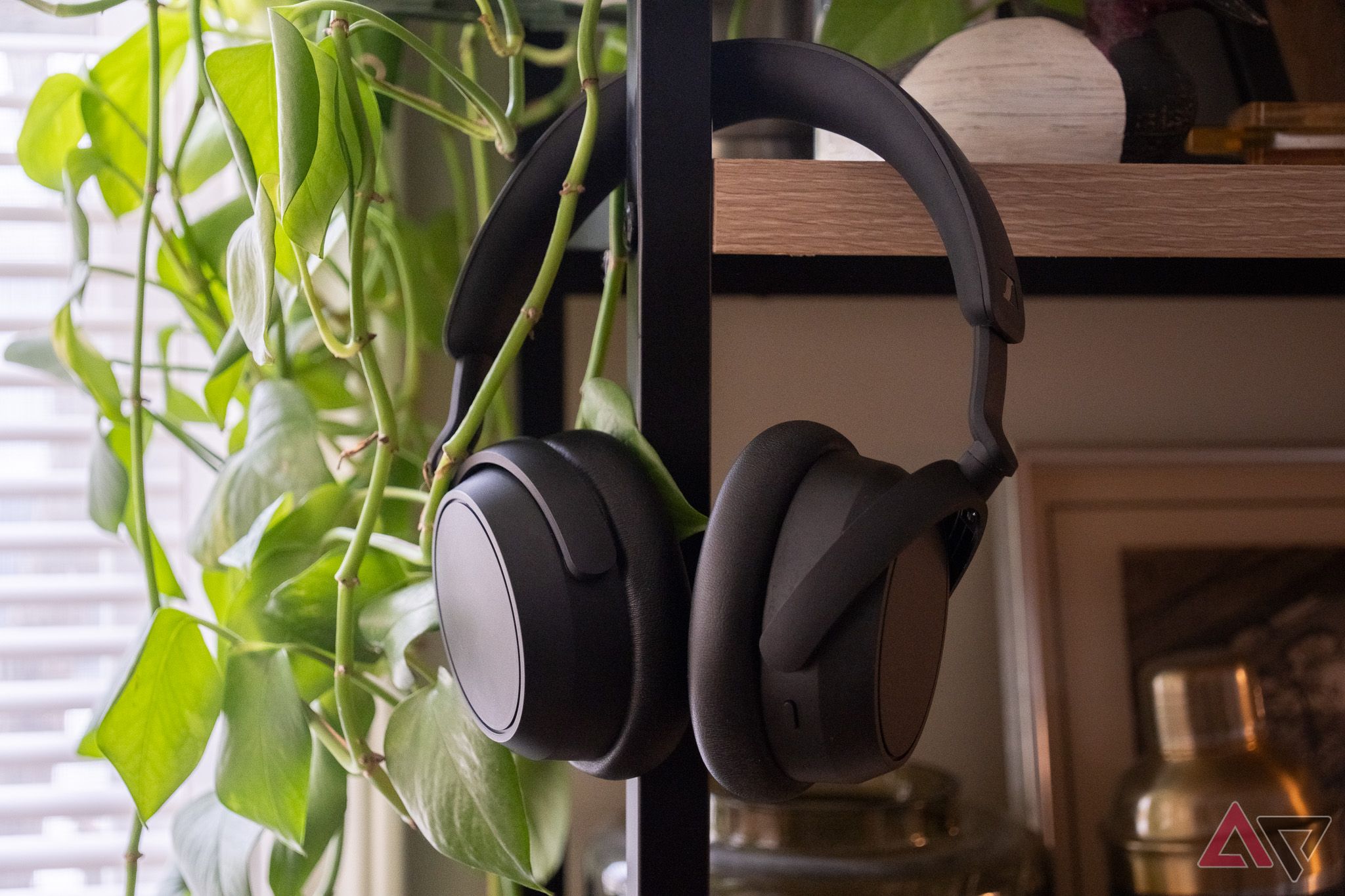 A pair of black headphones hanging from a shelf next to a plant