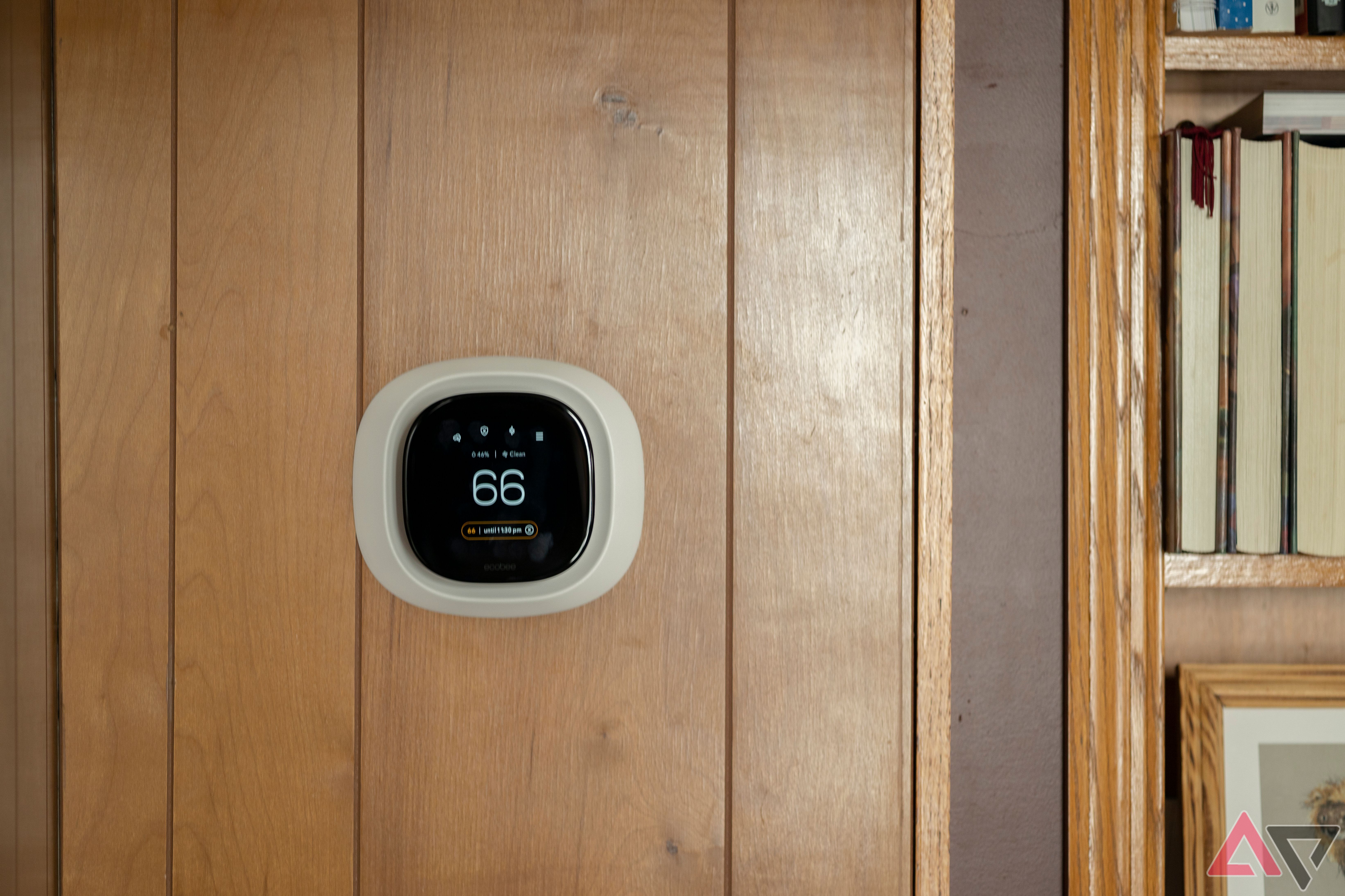 Ecobee Premium Smart Thermostat on wood paneled wall next to bookshelf