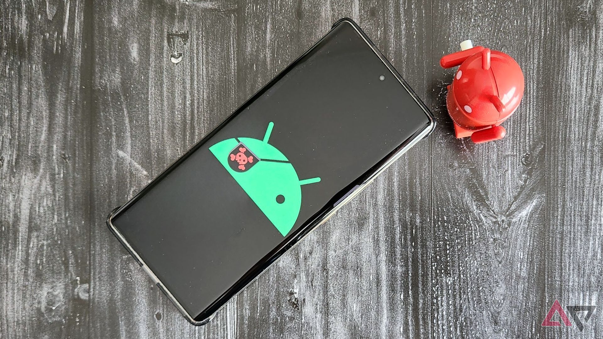 A phone with a pirate Android logo on a table next to a red Android figurine