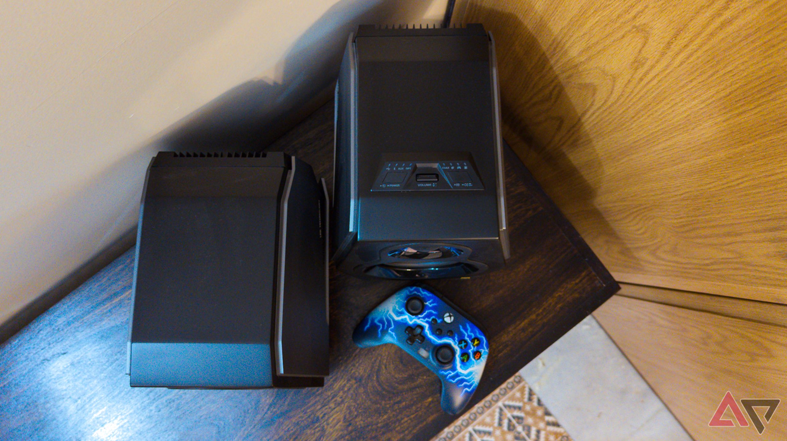 Top-down shot of the Hecate G5000 speakers with a game controller on a dark walnut wood shelf