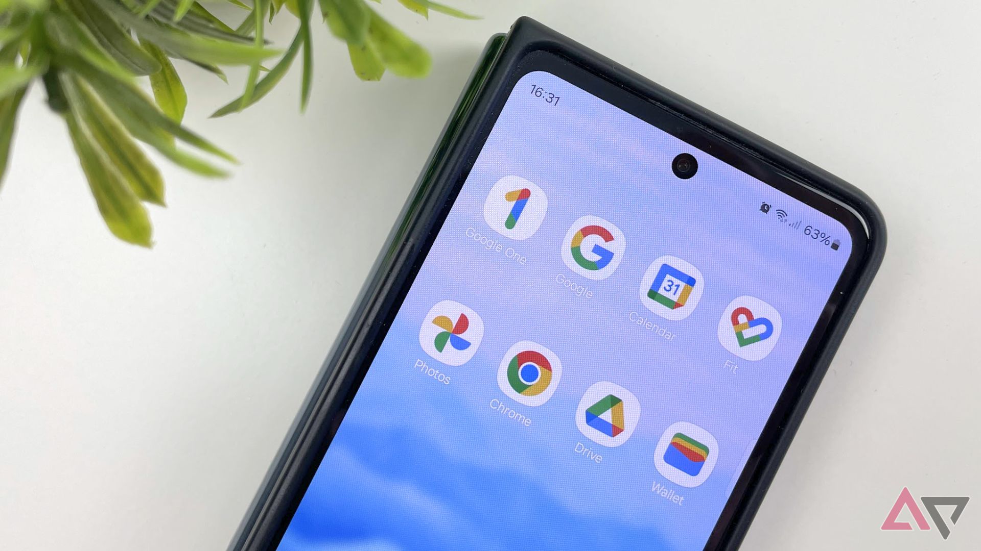 Google apps displayed on a homescreen with a plant beside the phone on a table