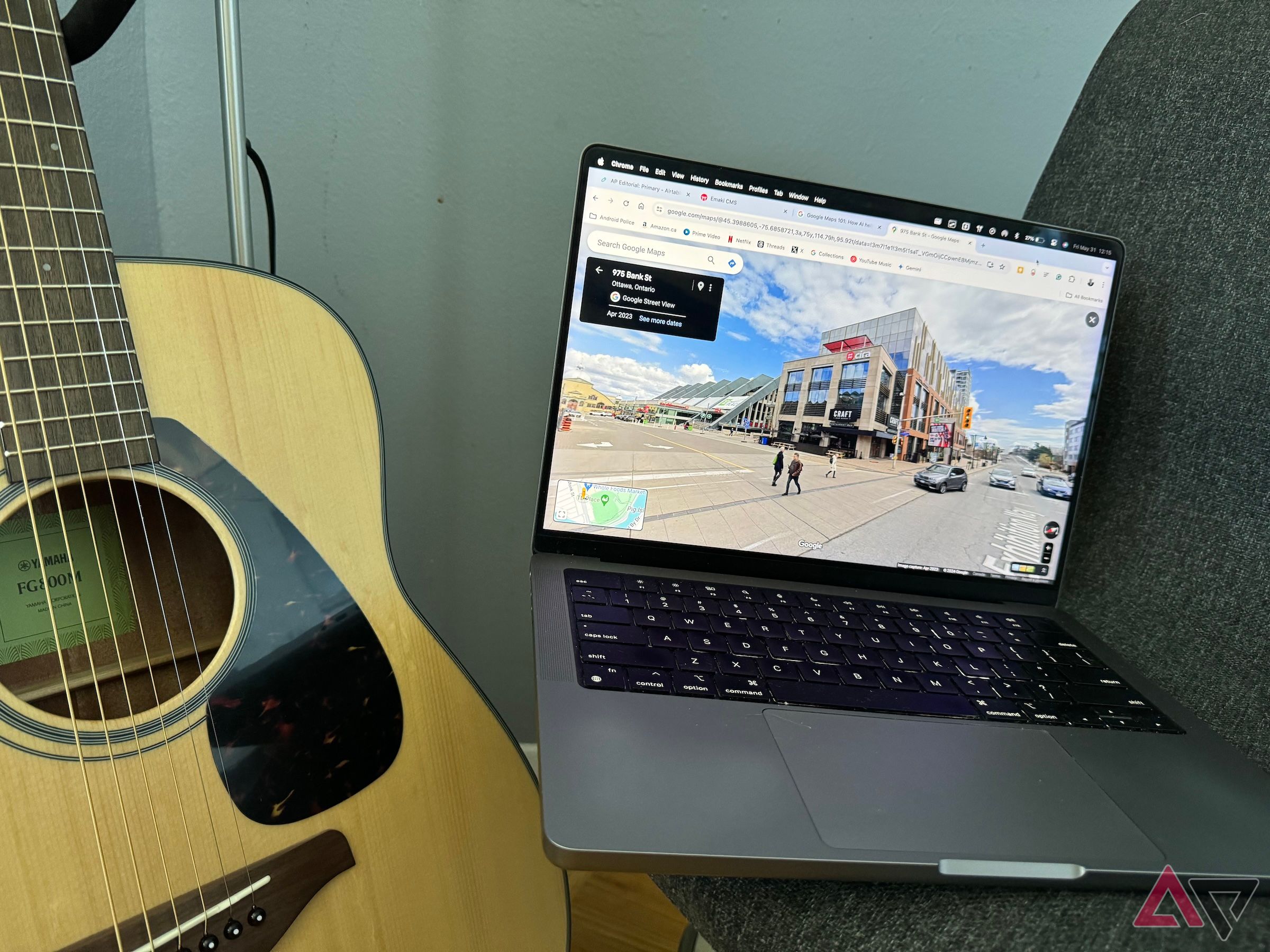 Streetview on a MacBook Pro that is sitting on a grey chair next to an acoustic guitar.