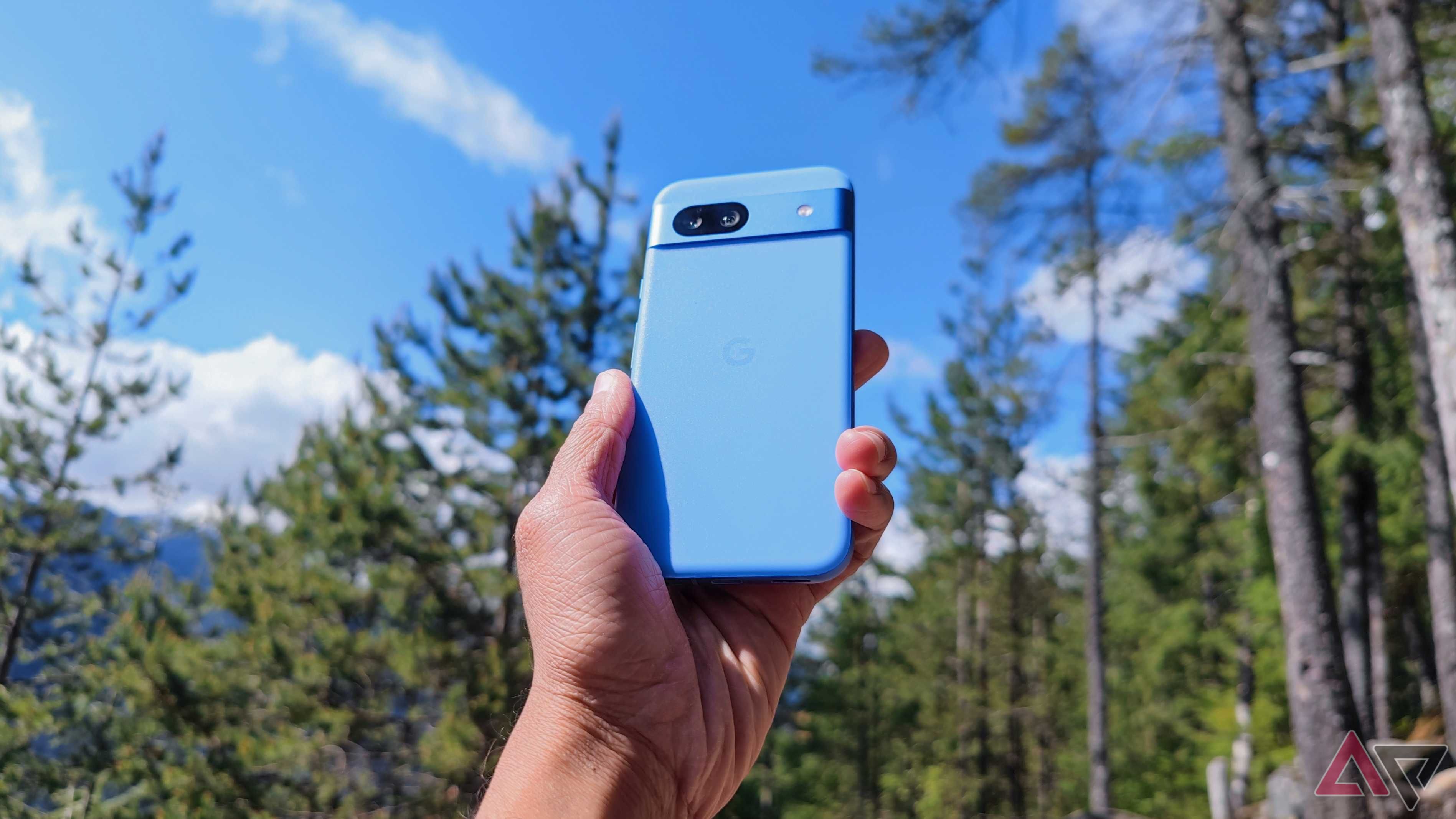 Google's Pixel 8a held against a sunny forest.