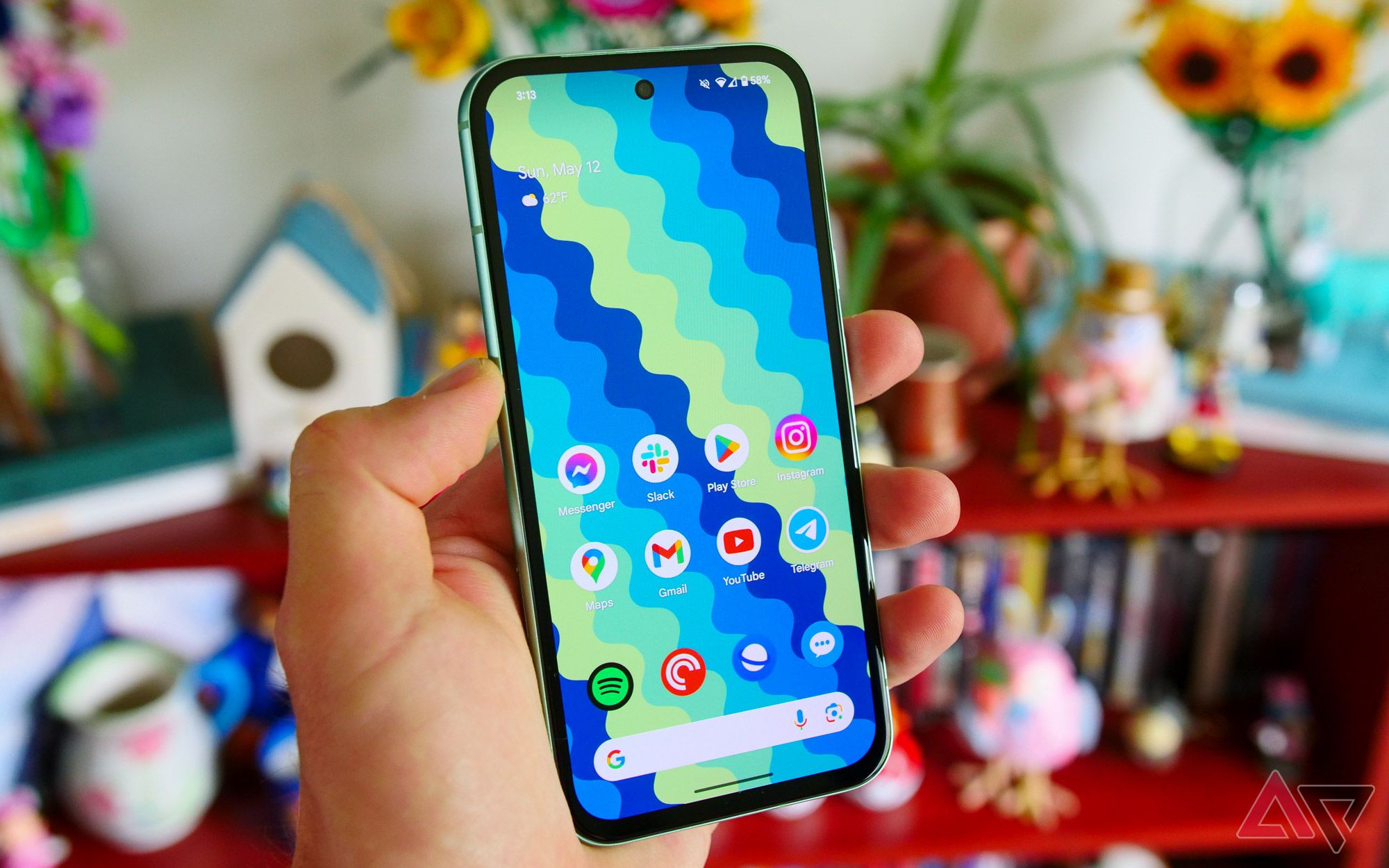 A Pixel 8a held in a hand with a bookshelf in the background.