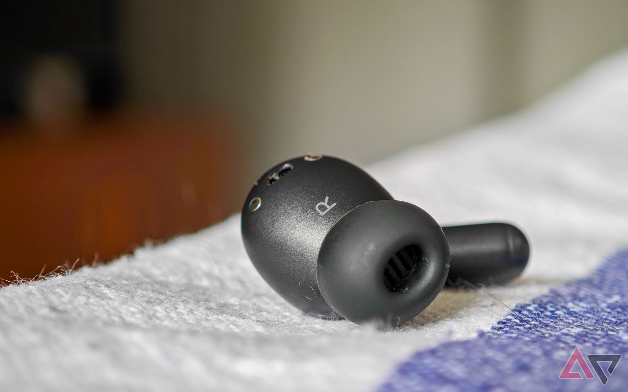 The Moto Buds+ in black, with the right earbud lying on a white and blue tablecloth