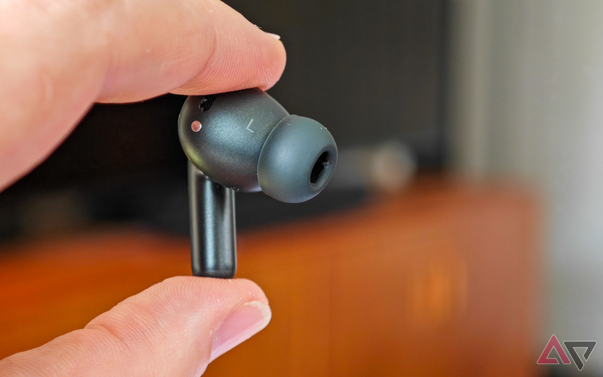 The Moto Buds+ in black, with the left earbud being held up between two fingers