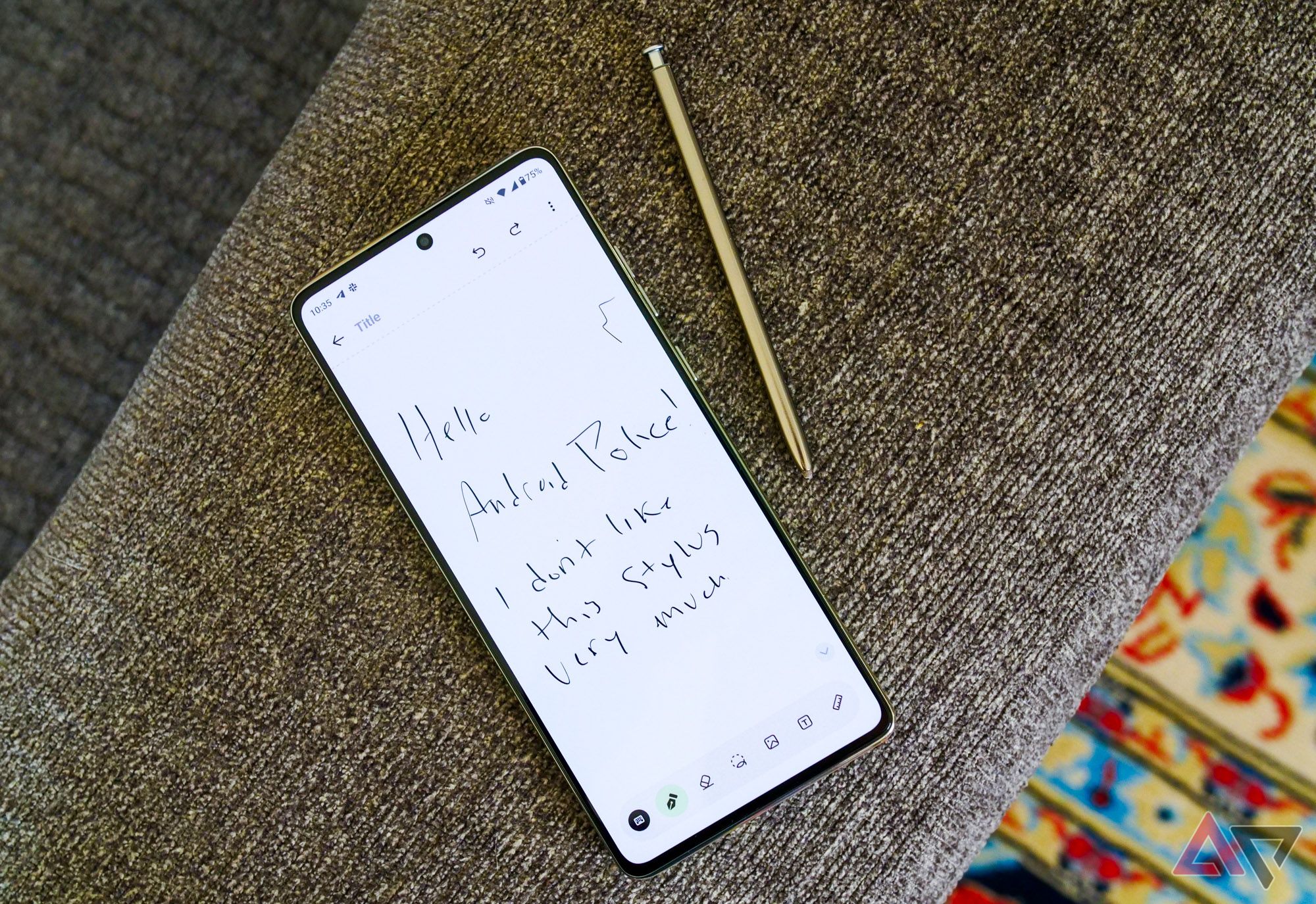 Moto G Stylus 2024 is sitting on the arm of the sofa and takes out the stylus. "Hello Android Police! I don't really like this stylus" written on the screen.