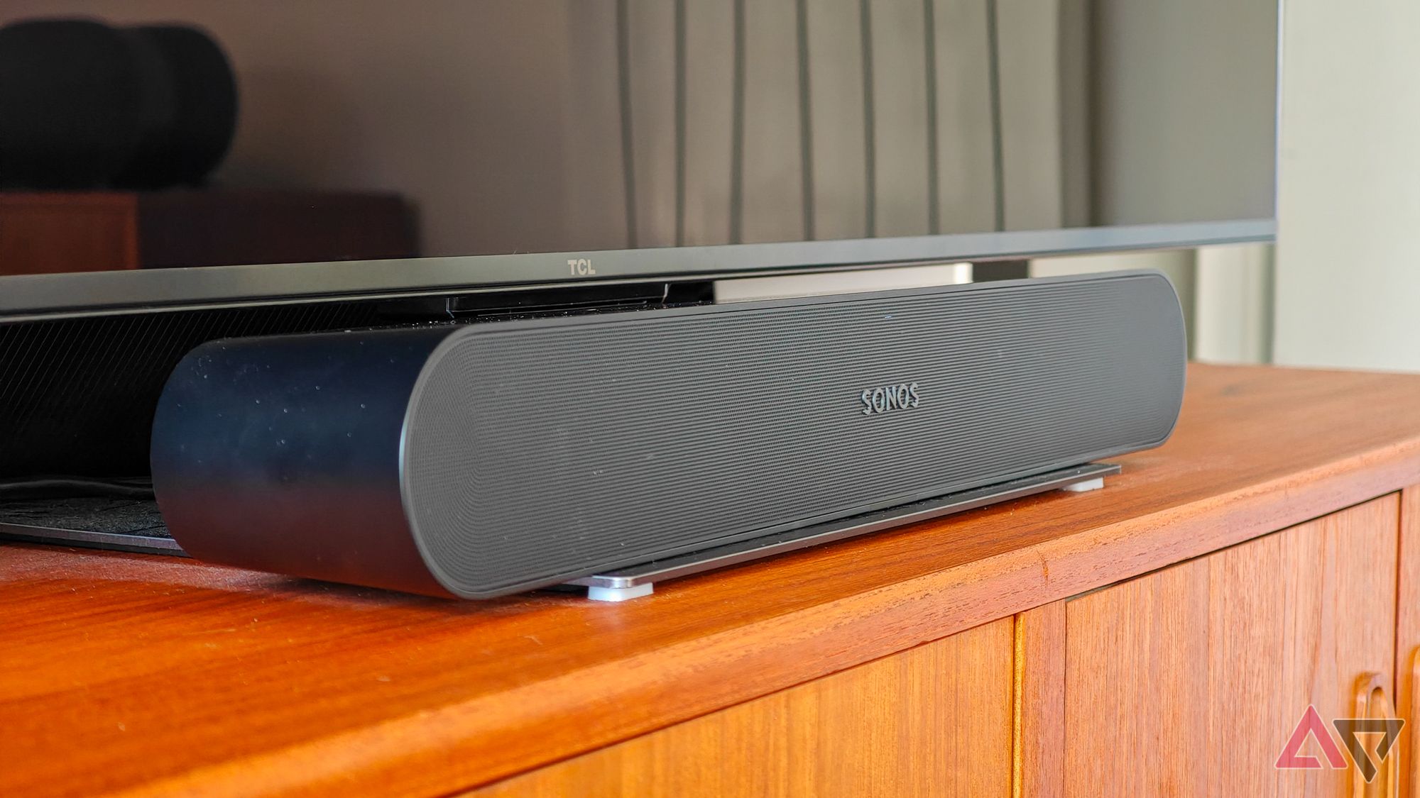 Sonos Ray soundbar on a wooden sideboard below a TV with a blank screen