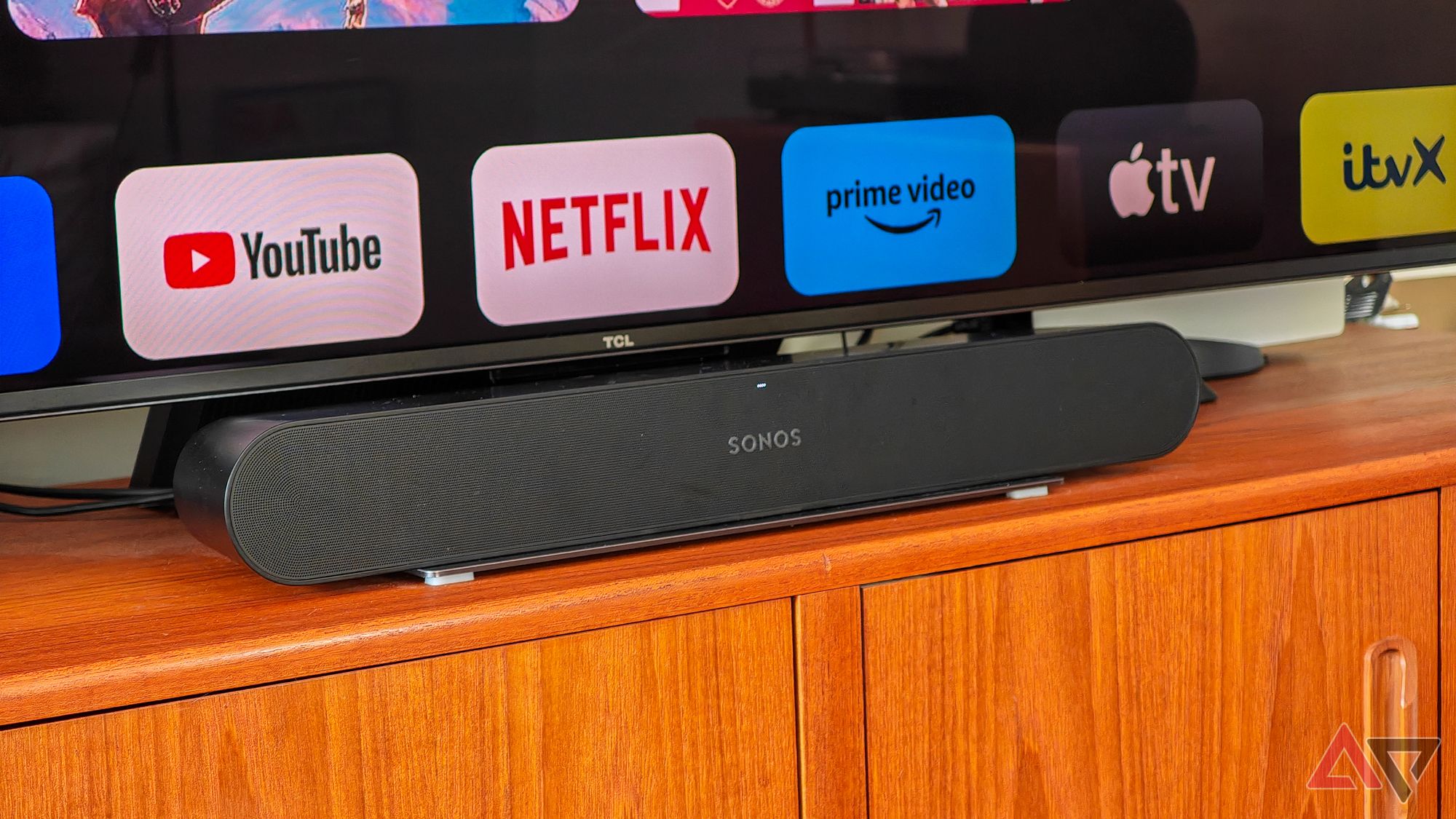 Sonos Ray on a wooden sideboard under a TV showing streaming app logos