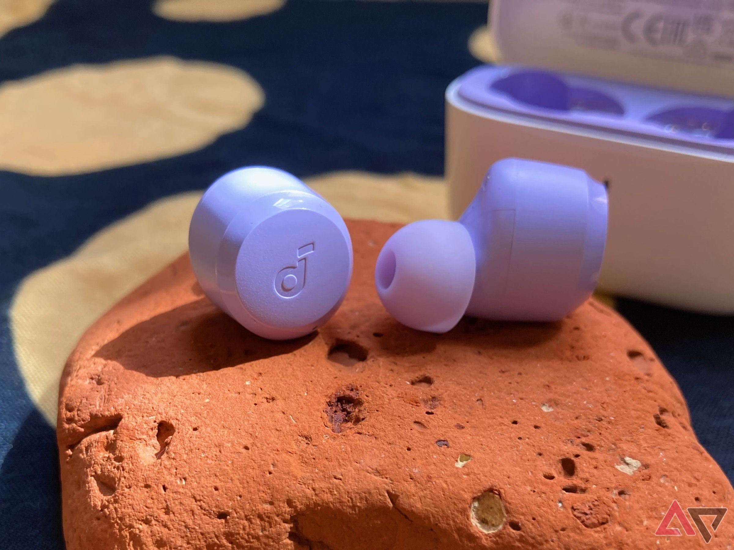 The Soundcore A20i earbuds sitting on top of a red rock with their case in the background