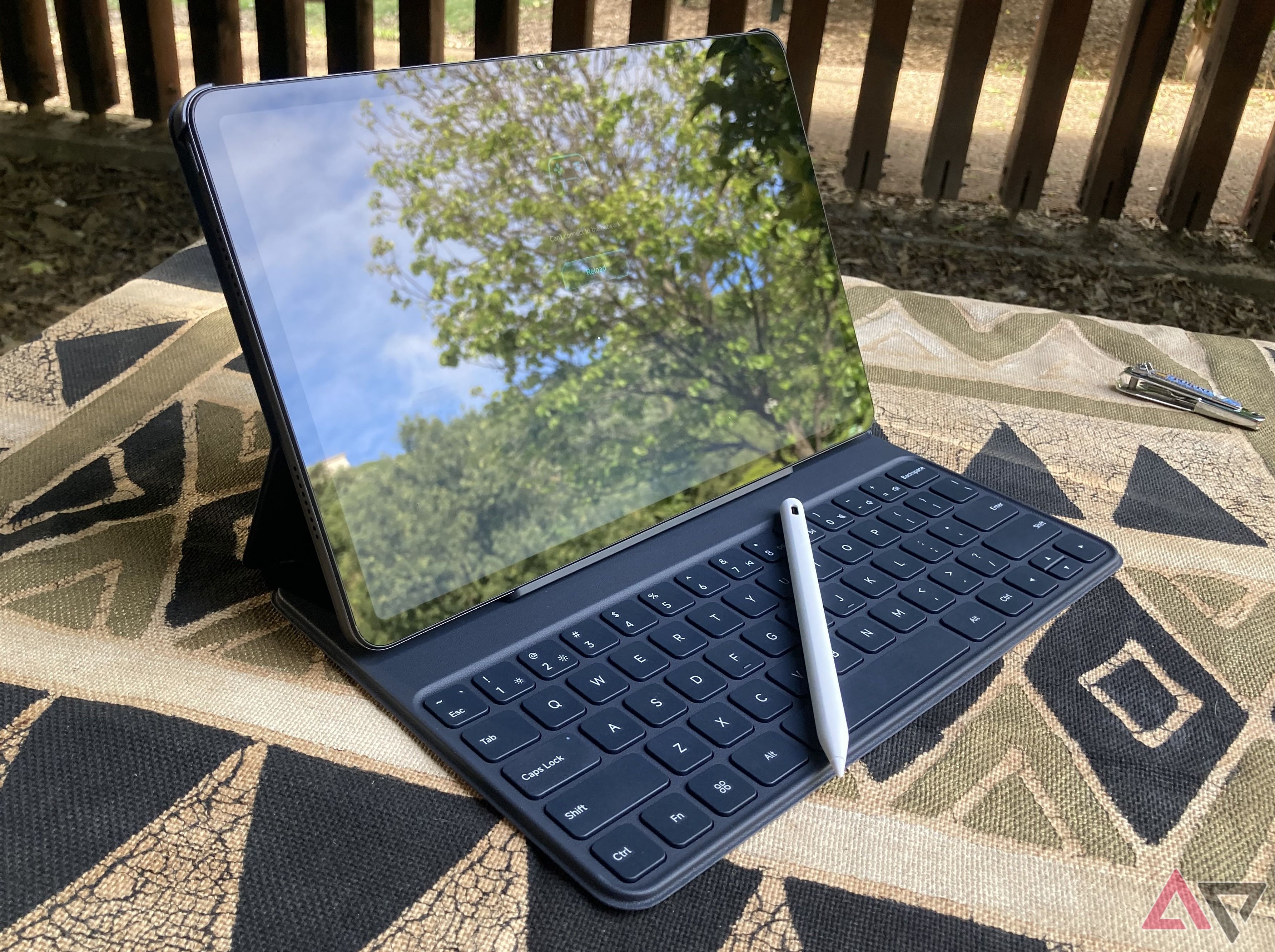 Xiaomi Redmi Pad Pro is placed on a covered picnic table with a keyboard attached and a stylus placed on it