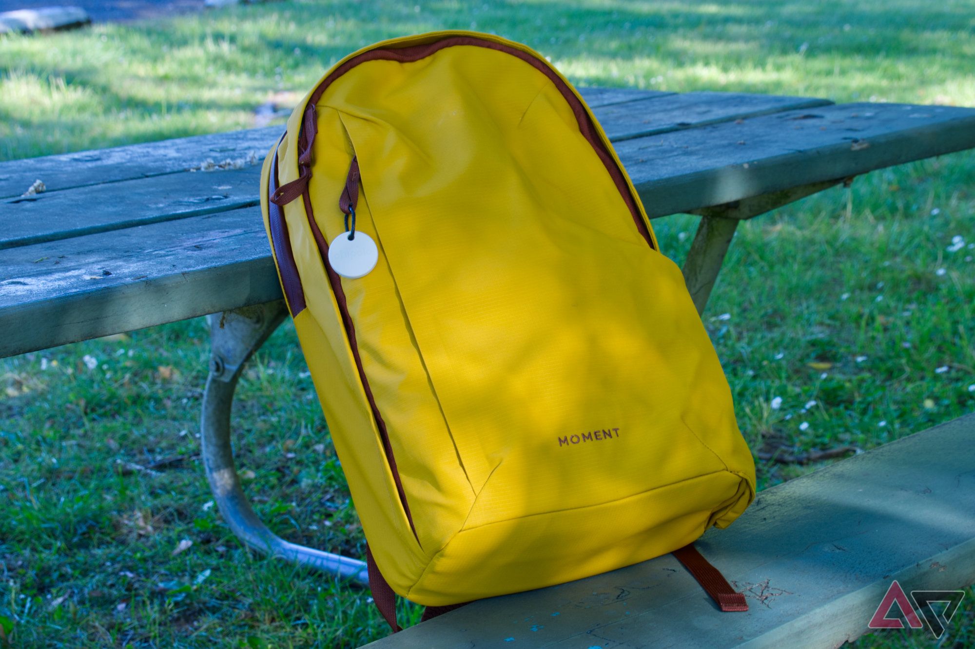 Chipolo One Point tag attached to a yellow backpack sitting on a park bench