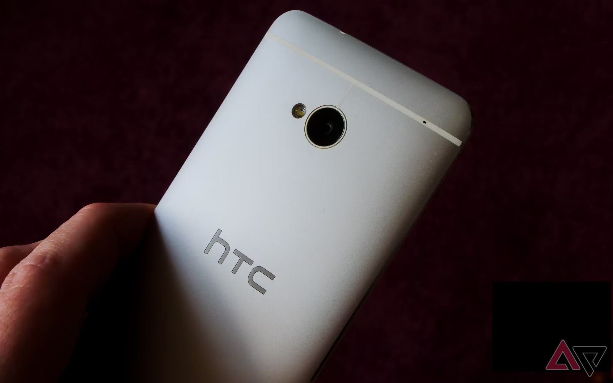 A hand holding an HTC One M7 against a dark black background.