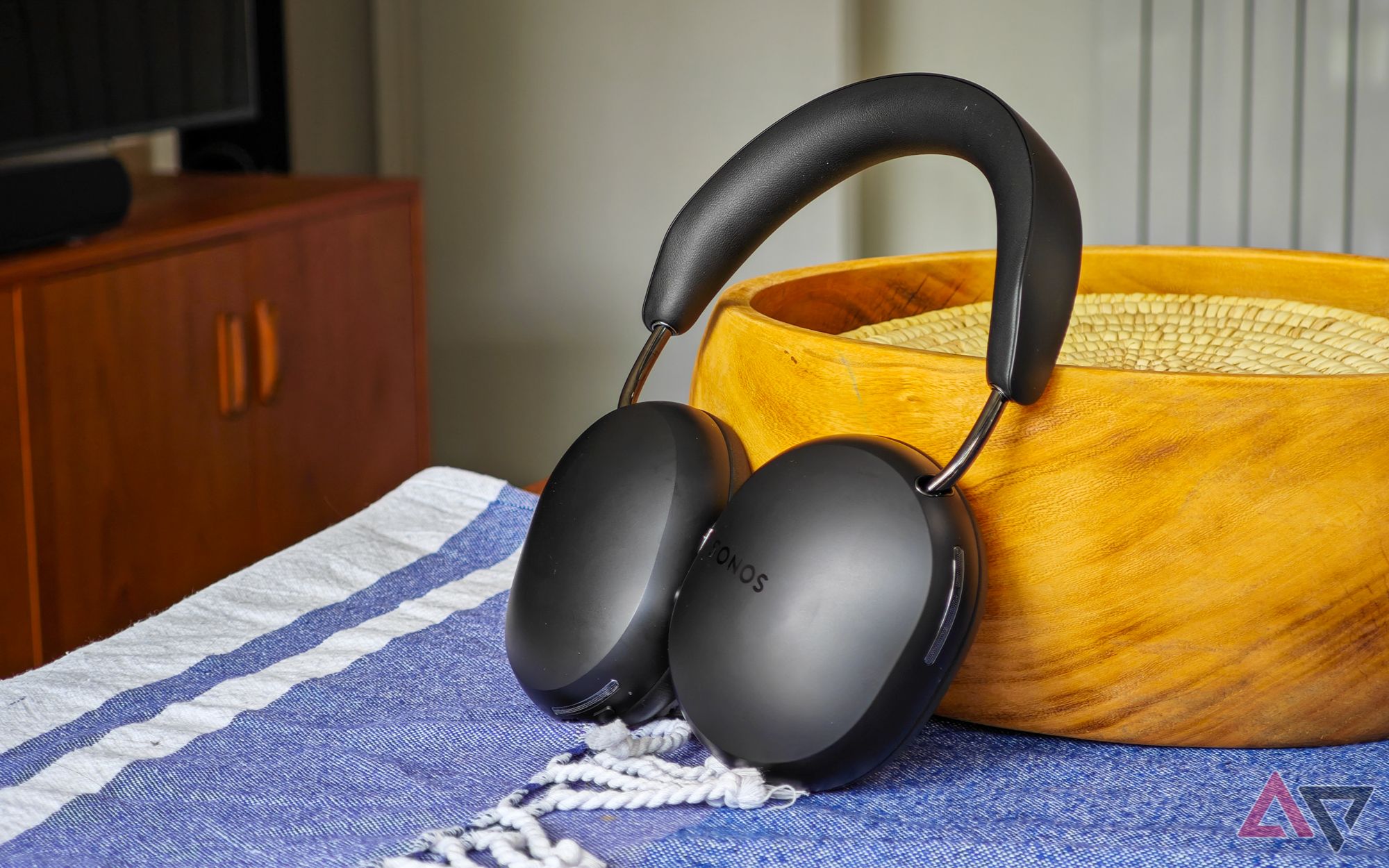 Sonos Ace headphones resting against a wooden bowl on a table with a blue tablecloth