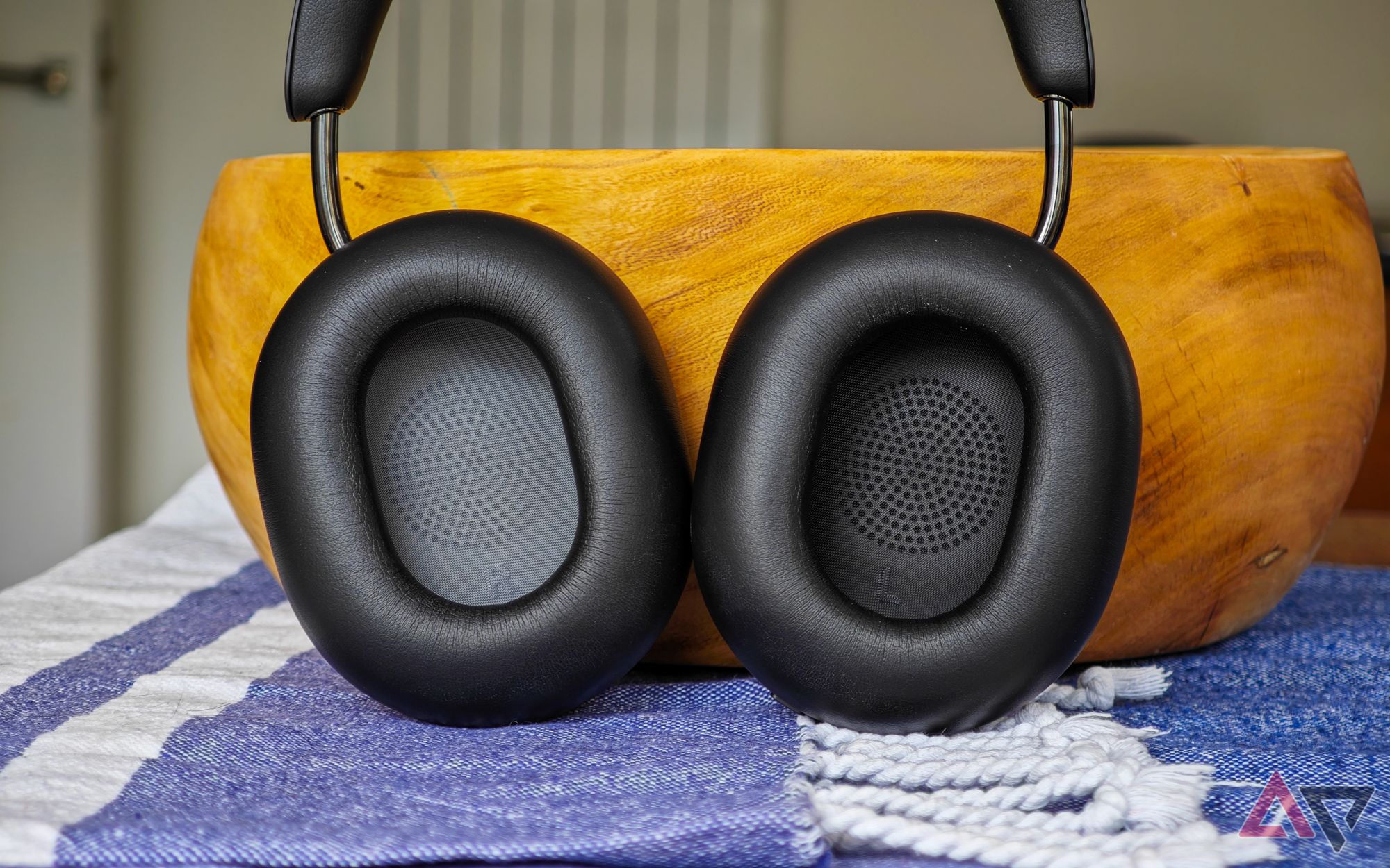 Sonos Ace headphones standing upright on a table, leaning against a wooden bowl, with the inner ear cups facing the camera