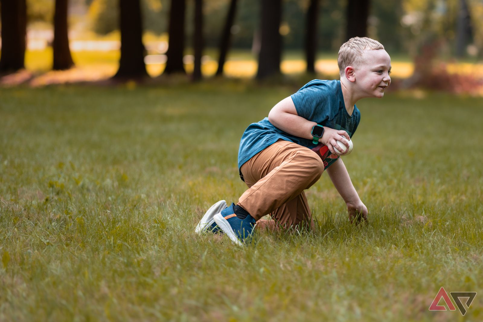 Child kneeling in grass, holding baseball and wearing the Garmin Bounce smartwatch