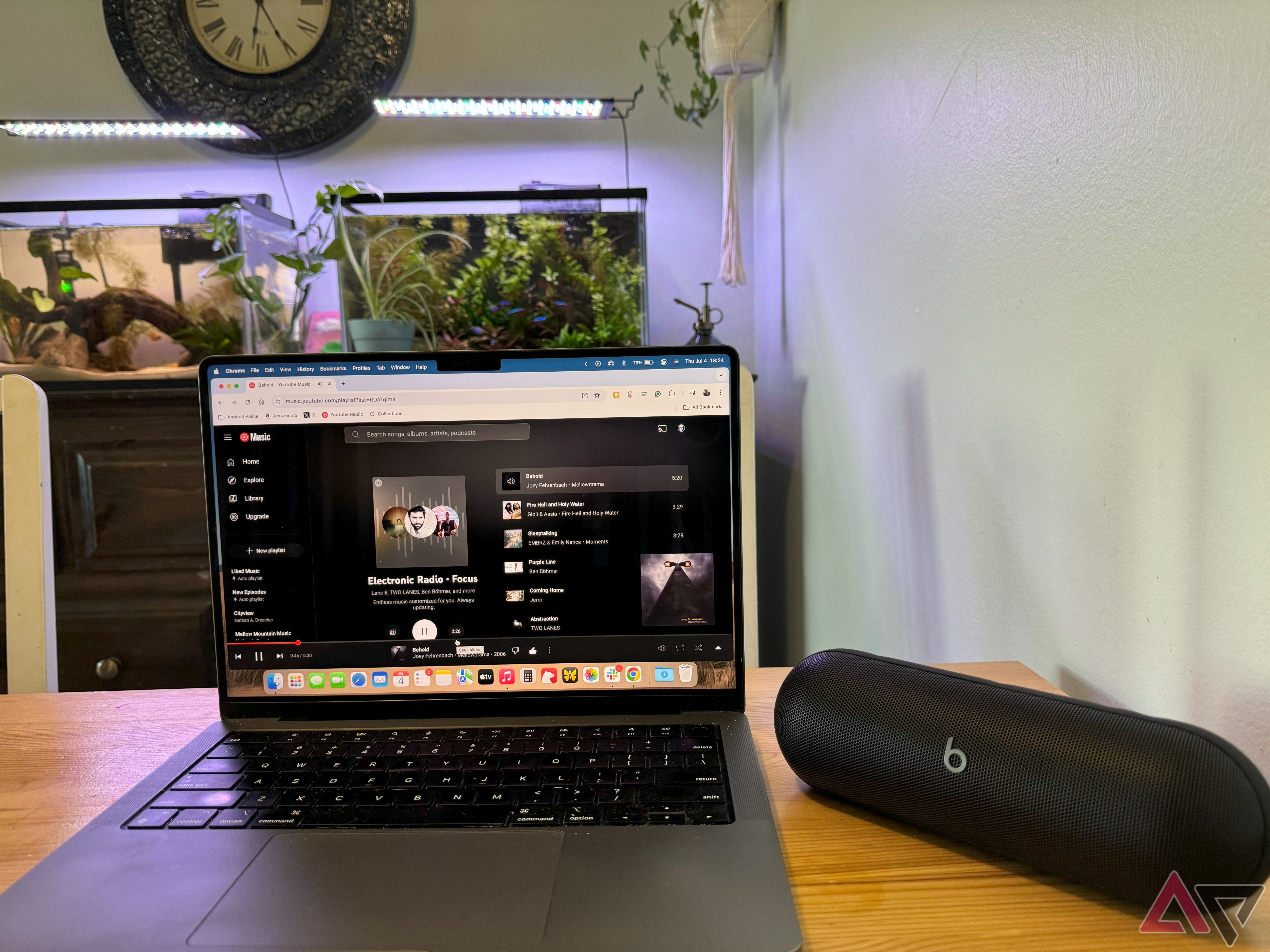 A black 2024 Beats Pill on a table next to a MacBook Pro with an aquarium behind them.