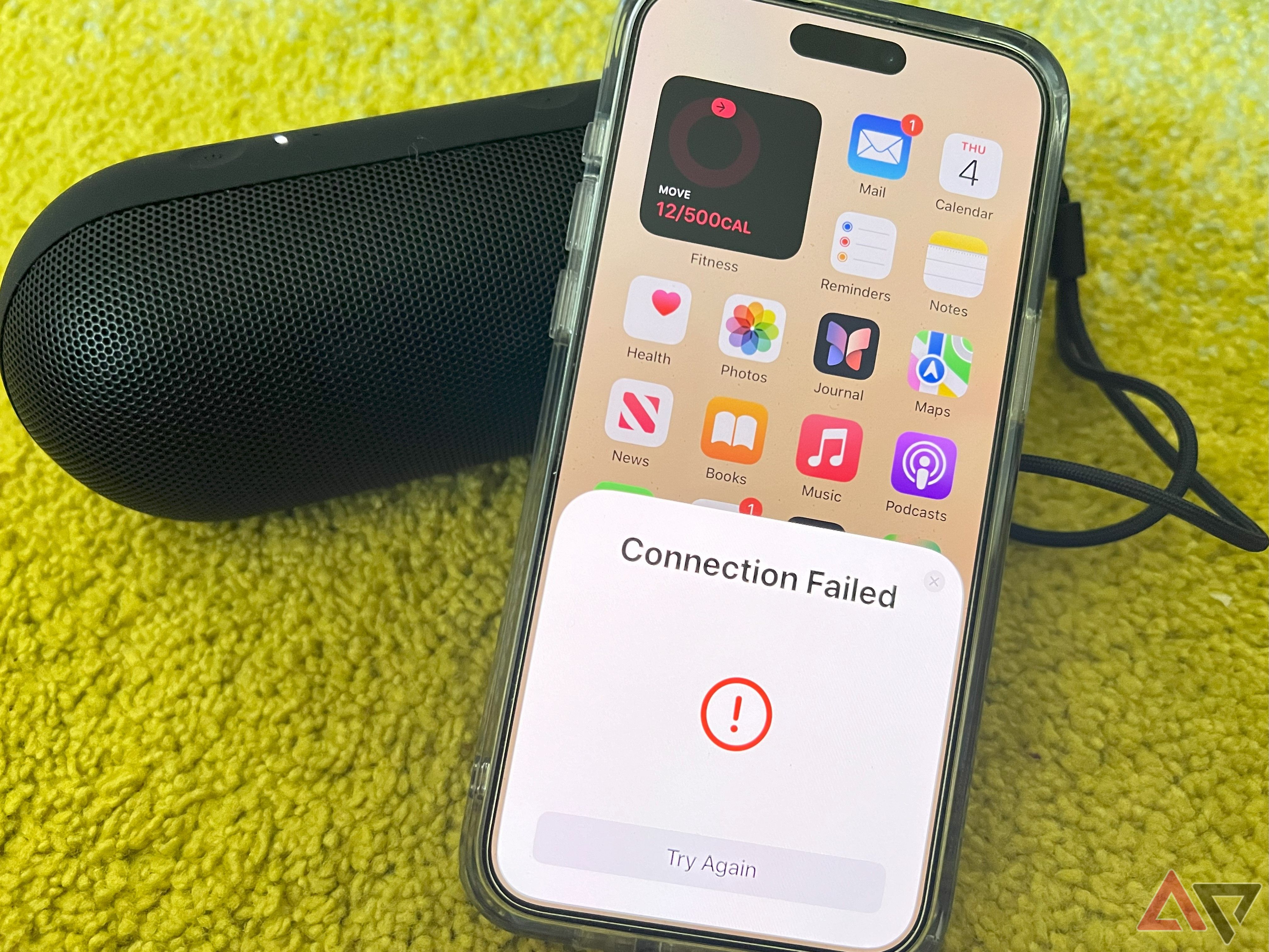 An iPhone showing a Connection Failed warning while resting against a black 2024 Beats Pill on a green carpet.