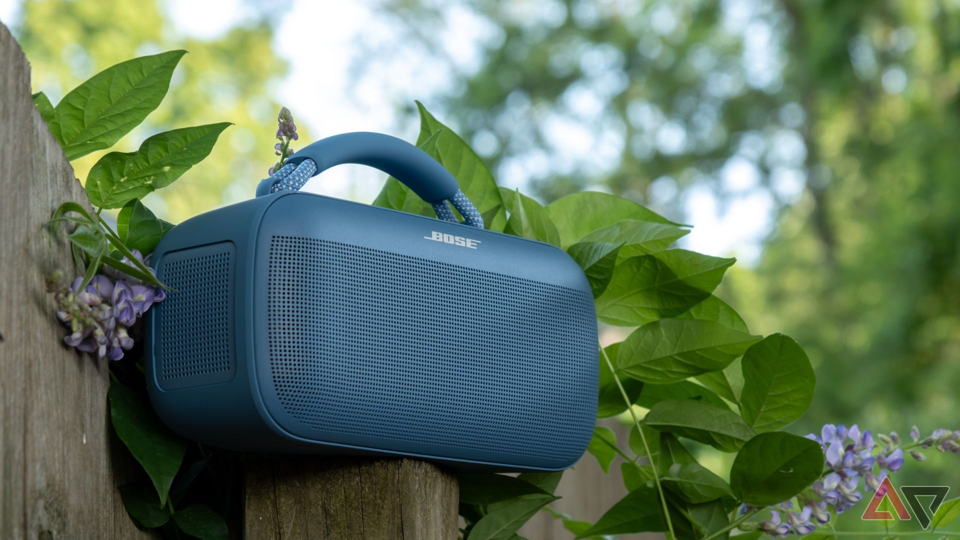 A Bose speaker sitting on a fence post, surrounded by foliage.