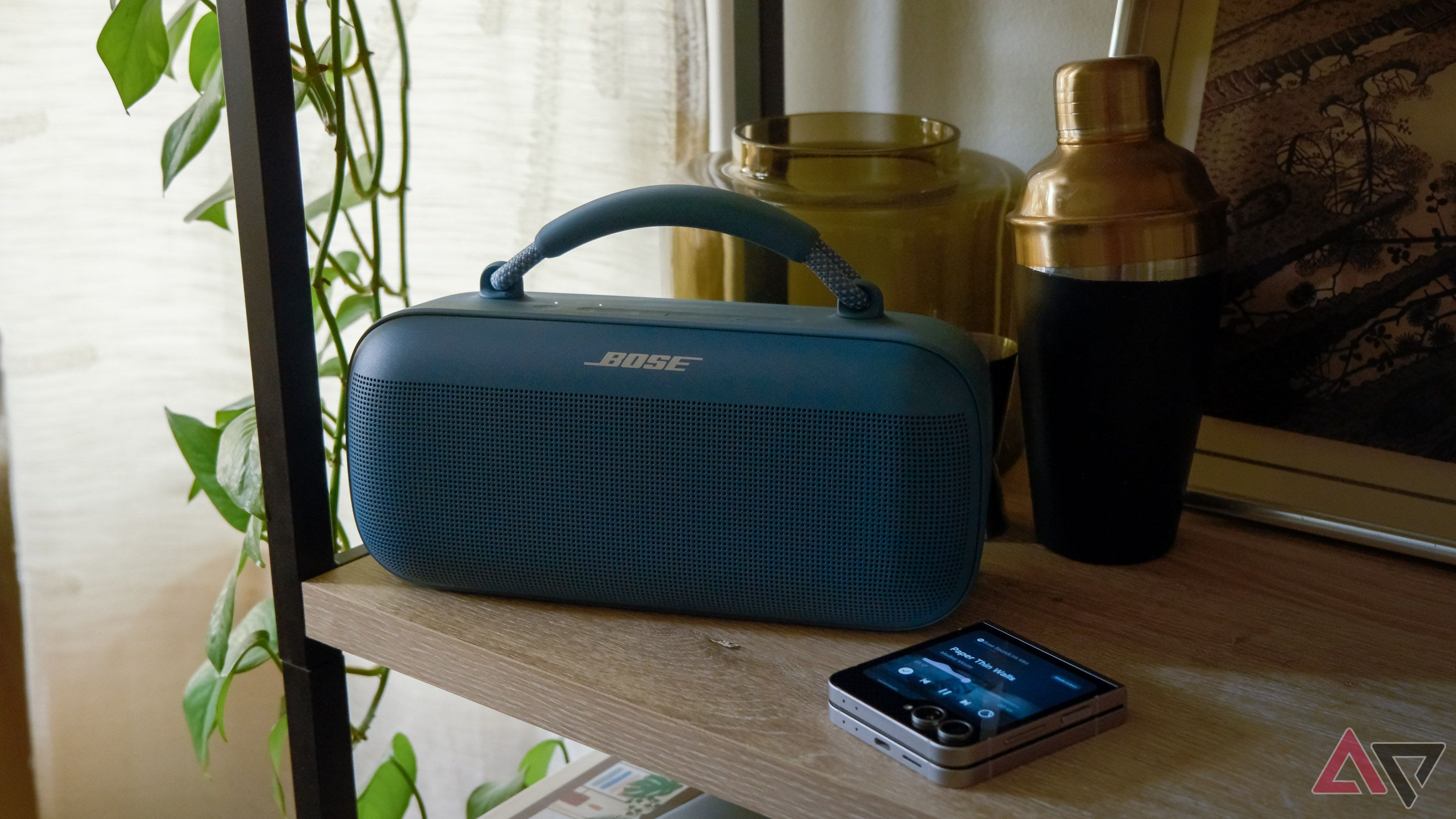 A Bluetooth speaker and a folding phone sitting on a shelf.