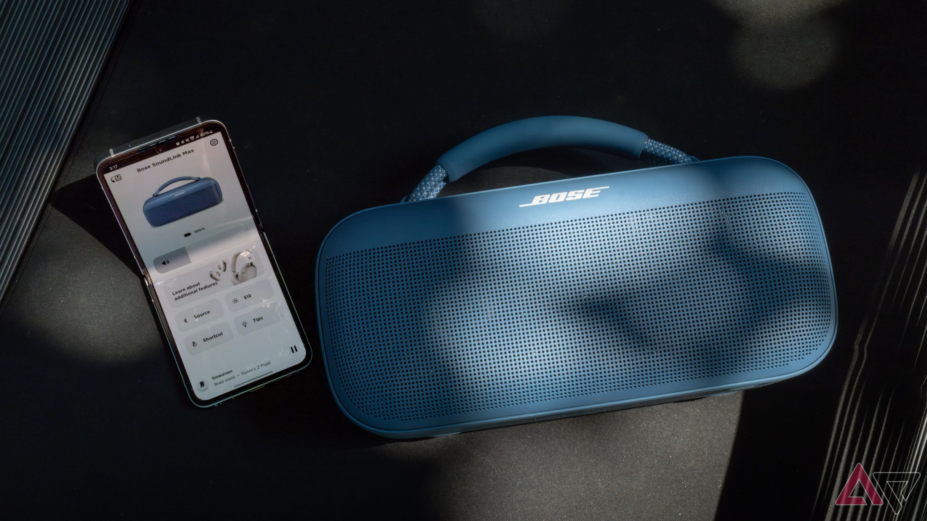 A Bose speaker next to a folding phone with the Bose app open.