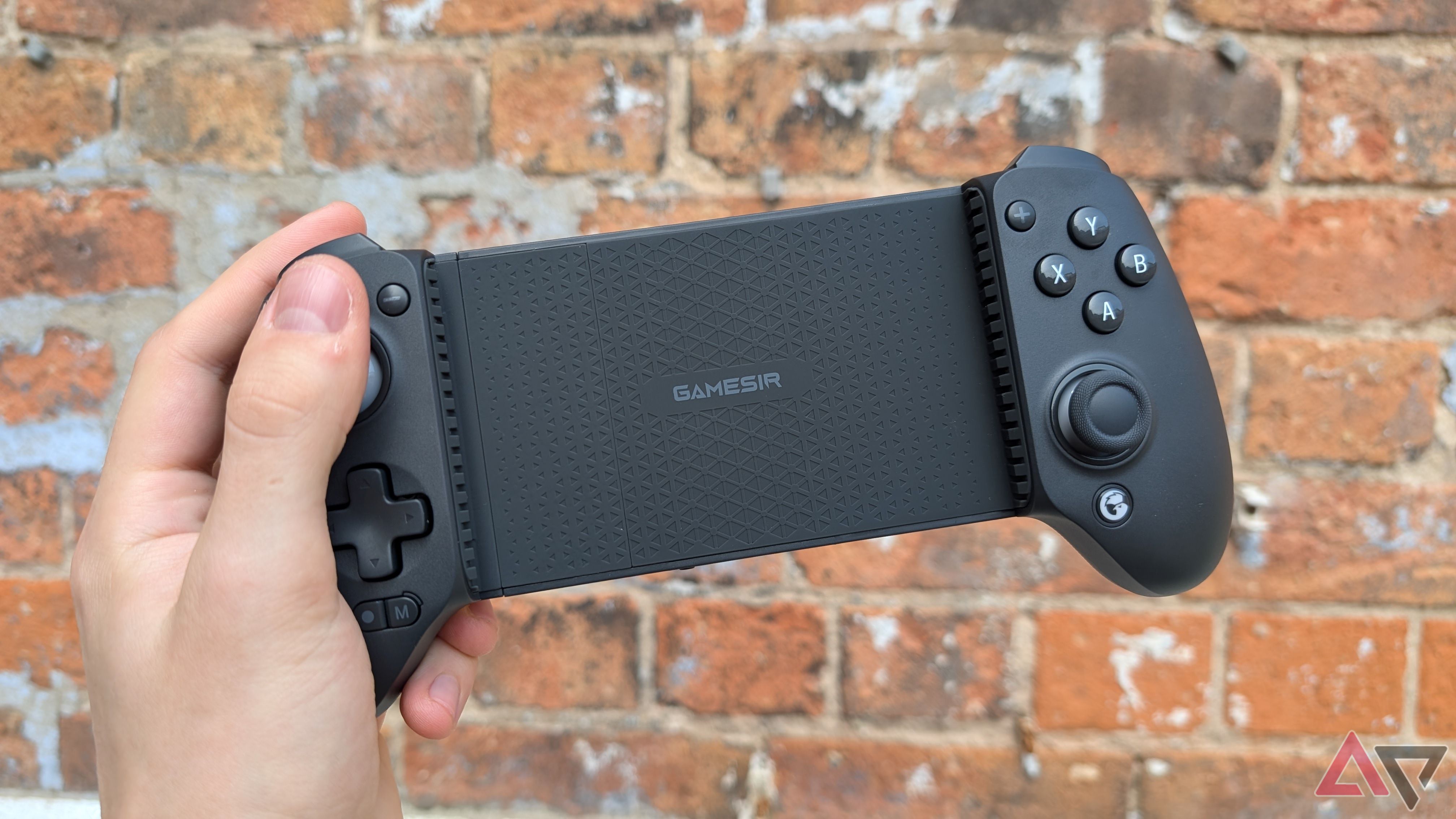 hand holding black game controller in front of brick wall