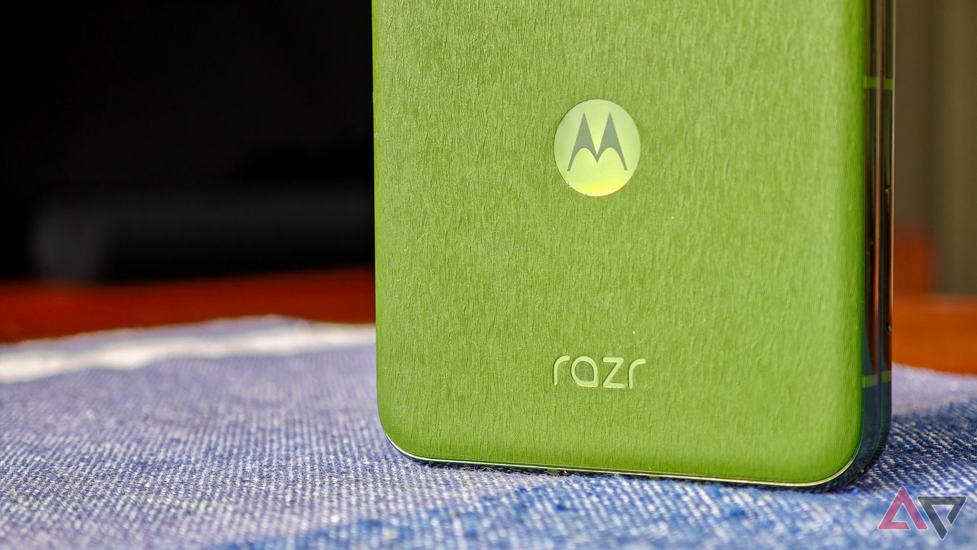 A closed Motorola Razr+ 2024 rests on a blue tablecloth, showing a close-up of the green back and Razr logo.