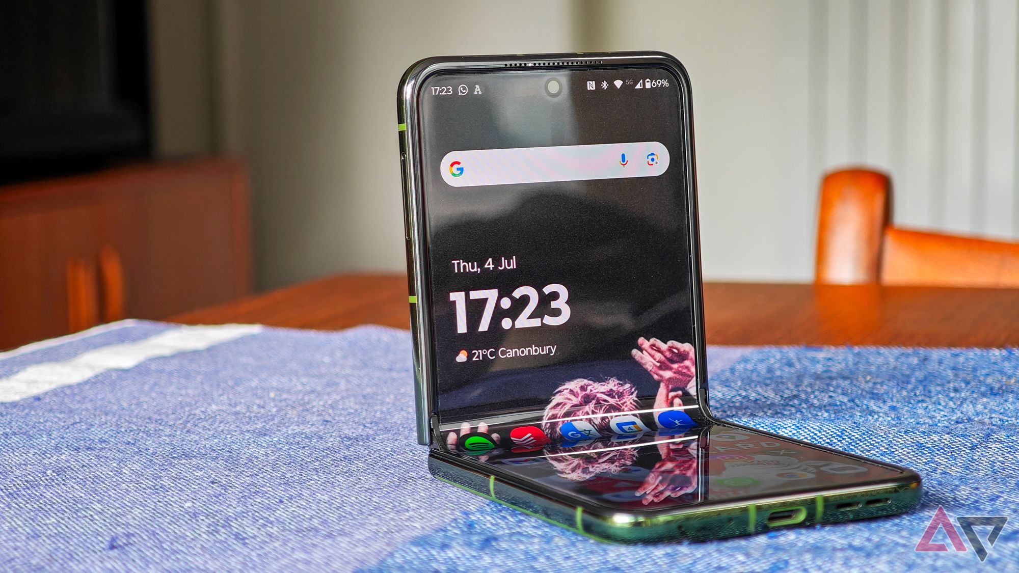 Motorola Razr+ 2024 resting on a blue tablecloth, half open, showing the Android homescreen