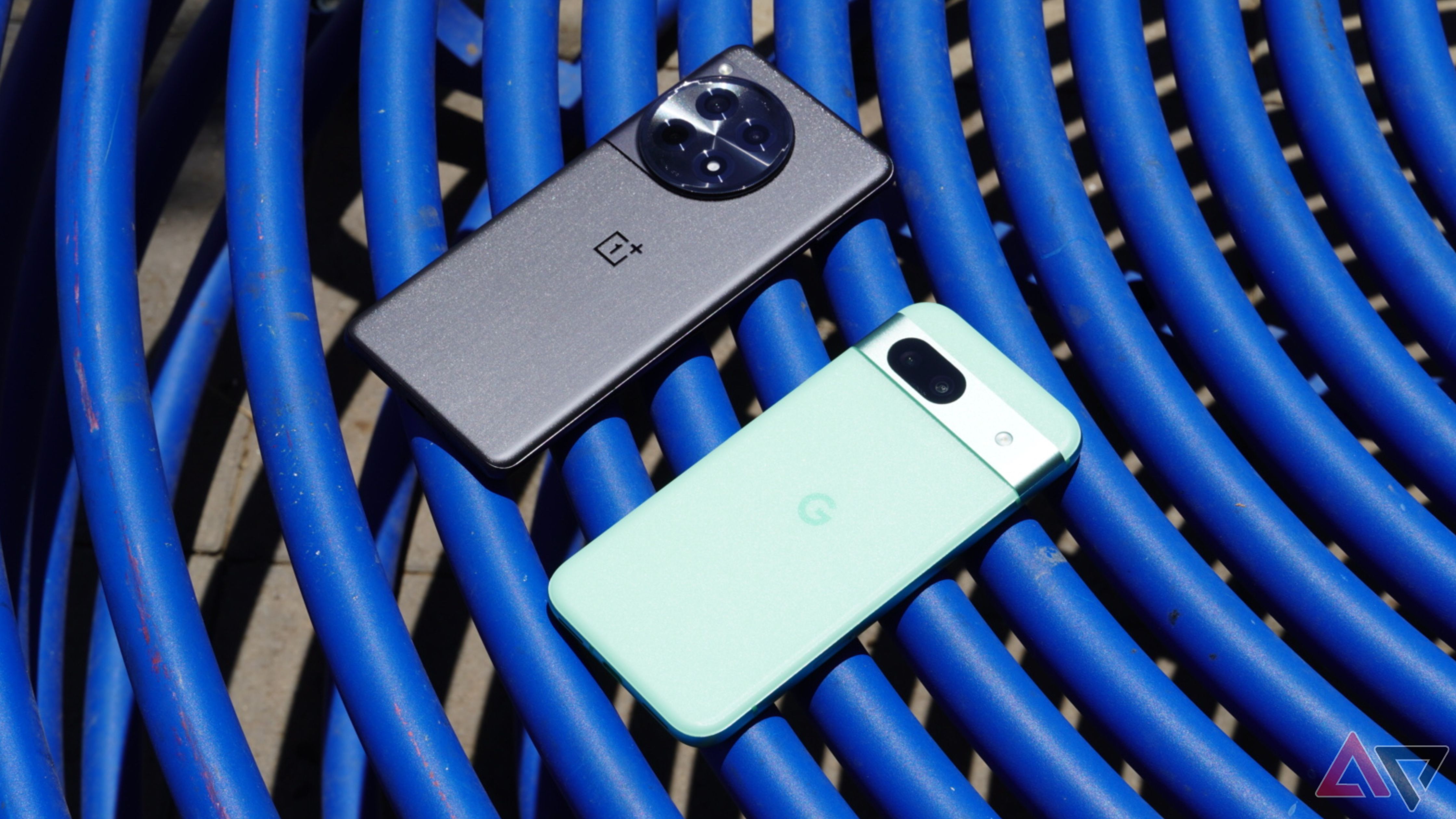 The OnePlus 12R and the Pixel 8a on a blue table outdoors.