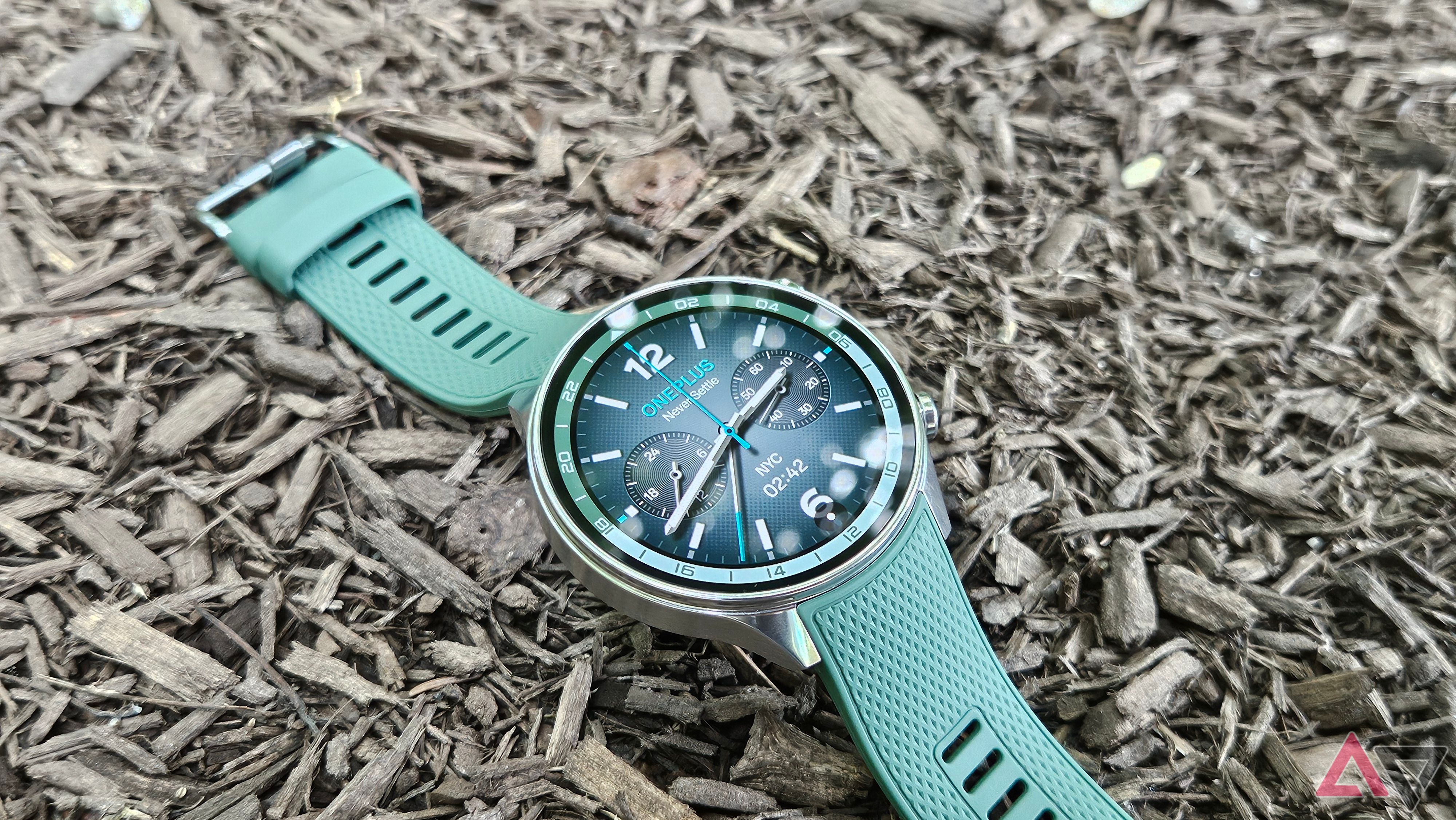 OnePlus Watch 2R in Forest Green resting on Mulch with an analogue clock