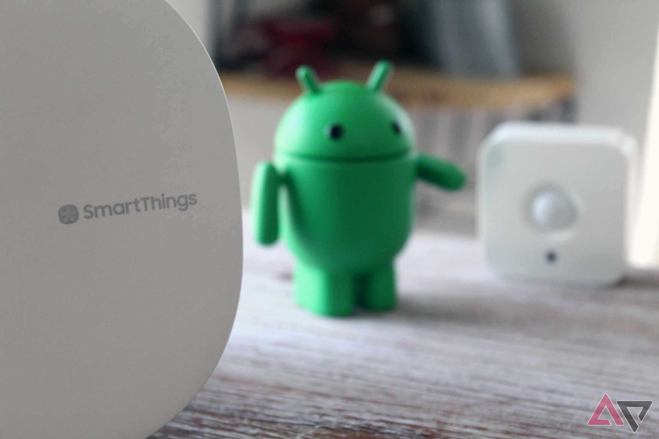 Photo of a Samsung SmartThings hub next to a Philips Hue motion sensor with an Android figurine between the two.