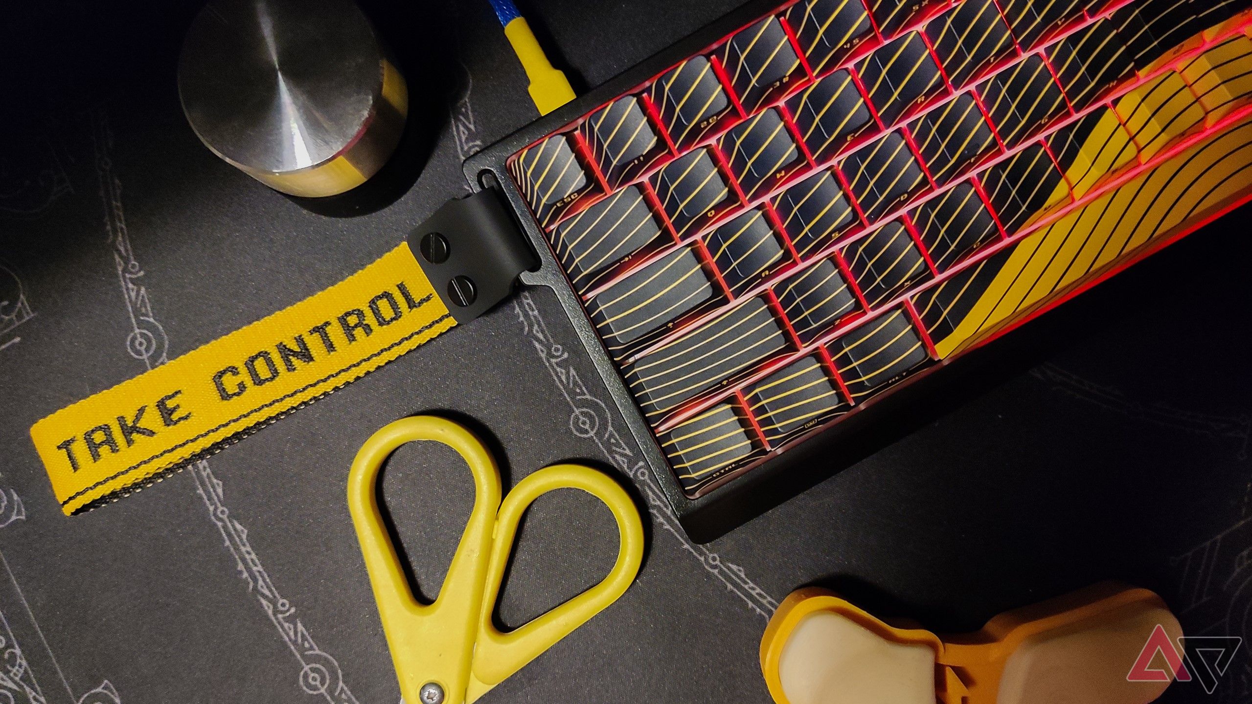 Flatlay of the Wooting 60HE+ on a black deskmat juxtaposed with a yellow scissor and wrist rest