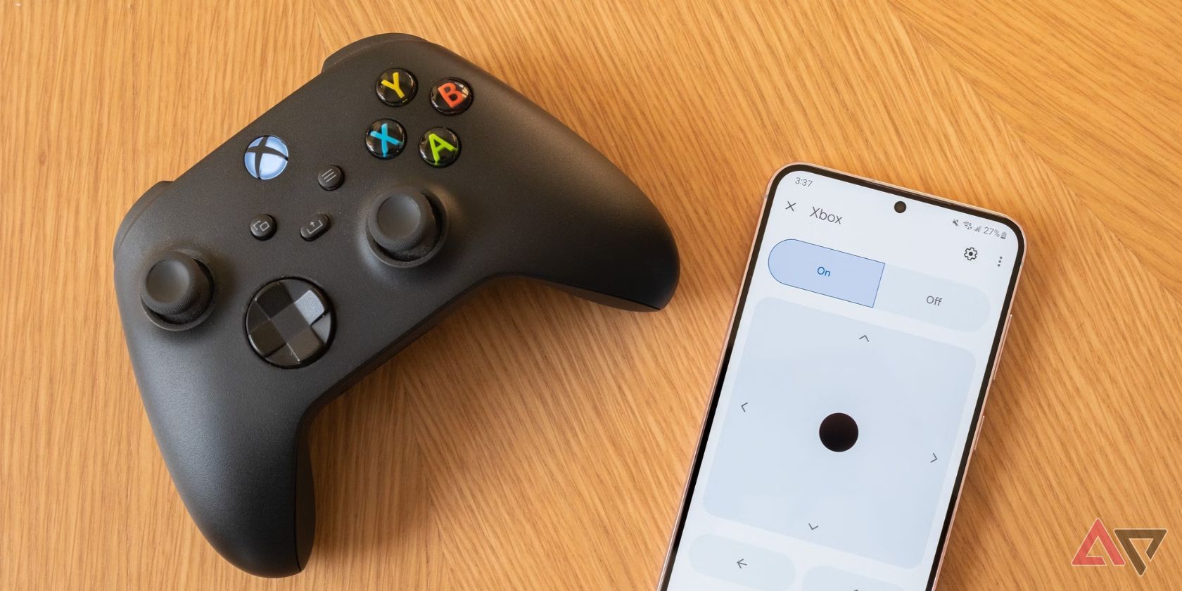 black game controller on light wood surface next to phone