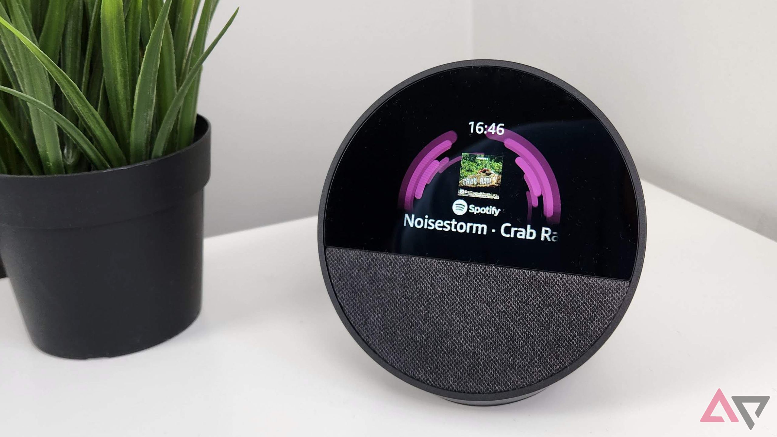 Amazon Echo Spot trên chiếc bàn trắng cạnh một cái cây xanh đang hiển thị màn hình phát lại âm thanh