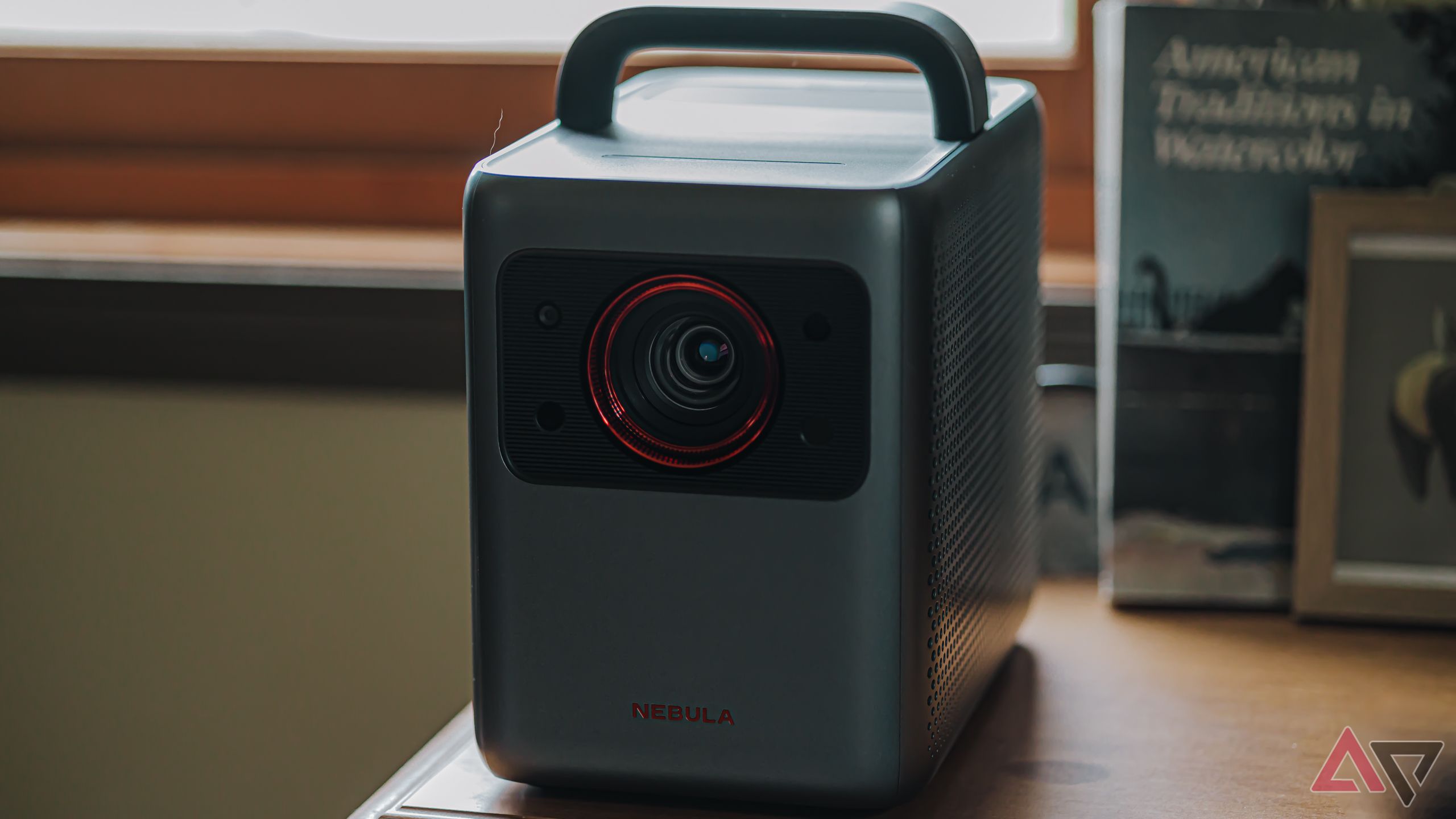 Anker Nebula Cosmos 4K Projector sitting on a wooden table with a lamp