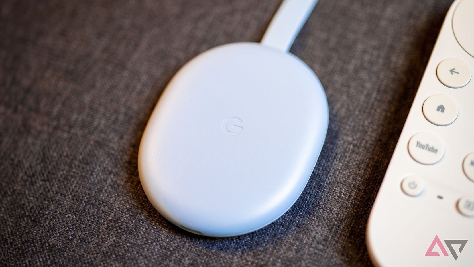 The Chromecast with Google TV HD sitting next to its remote on a couch.