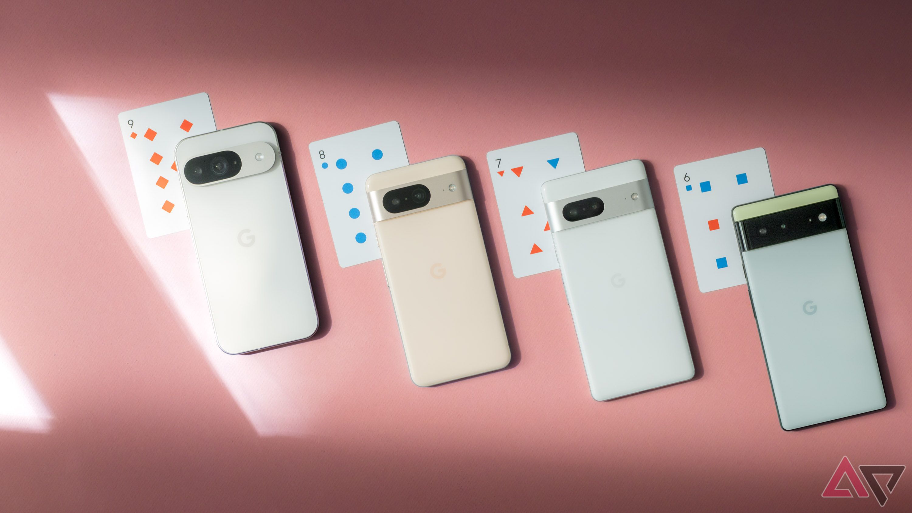 Four Google Pixel smartphones lined up on a pink surface next to playing cards