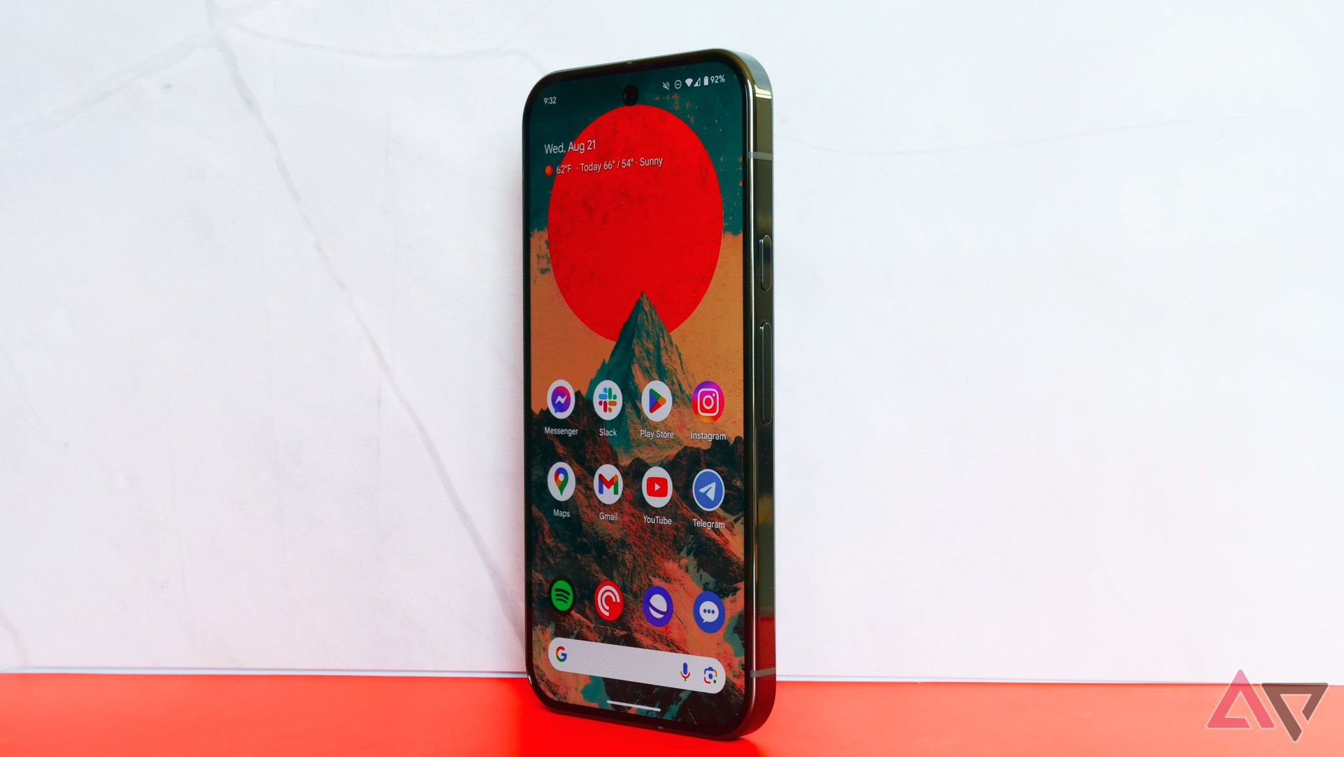 The Pixel 9 Pro standing up on an orange and white backdrop with the home screen showing.